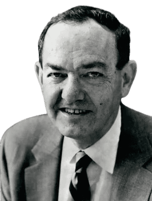 A black-and-white portrait of a man with a friendly, approachable smile, wearing a suit, white shirt, and striped tie. His relaxed expression and professional attire suggest he is an accomplished academic or business professional, likely from the mid-20th century. The background, with bookshelves, adds an intellectual context to the image.