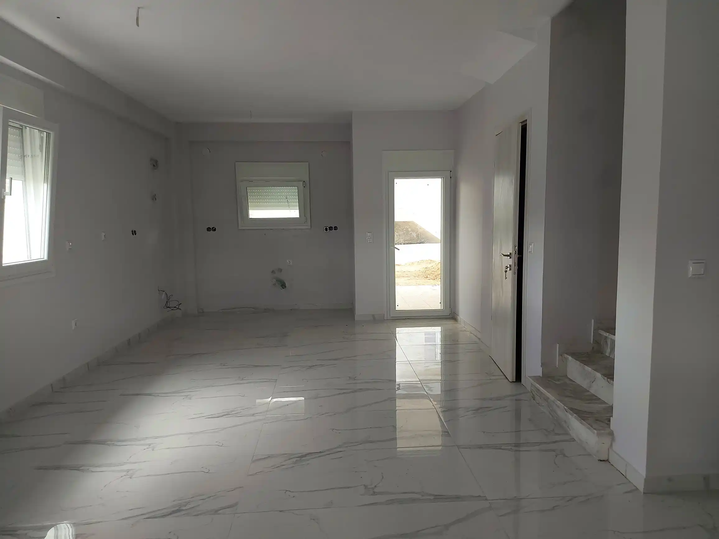 Άδειο μοντέρνο σαλόνι με γυαλιστερό μαρμάρινο δάπεδο, εσωτερική σκάλα και πρόσβαση σε εξωτερικό χώρο.