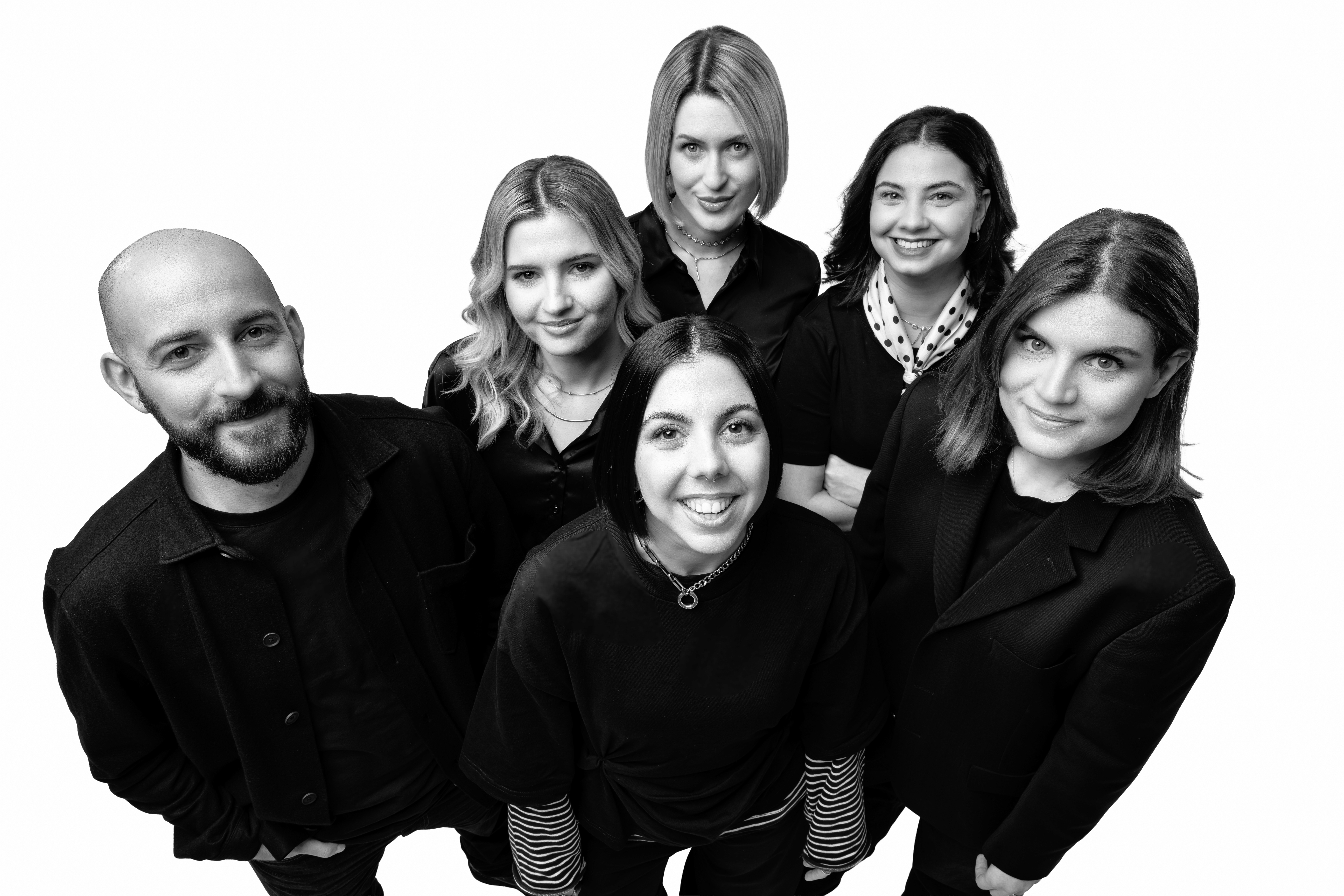 Black and white image of people working at a table with laptops, showing hands gesturing during discussion of digital content displayed on screens, with fabrica® logo in the corner.