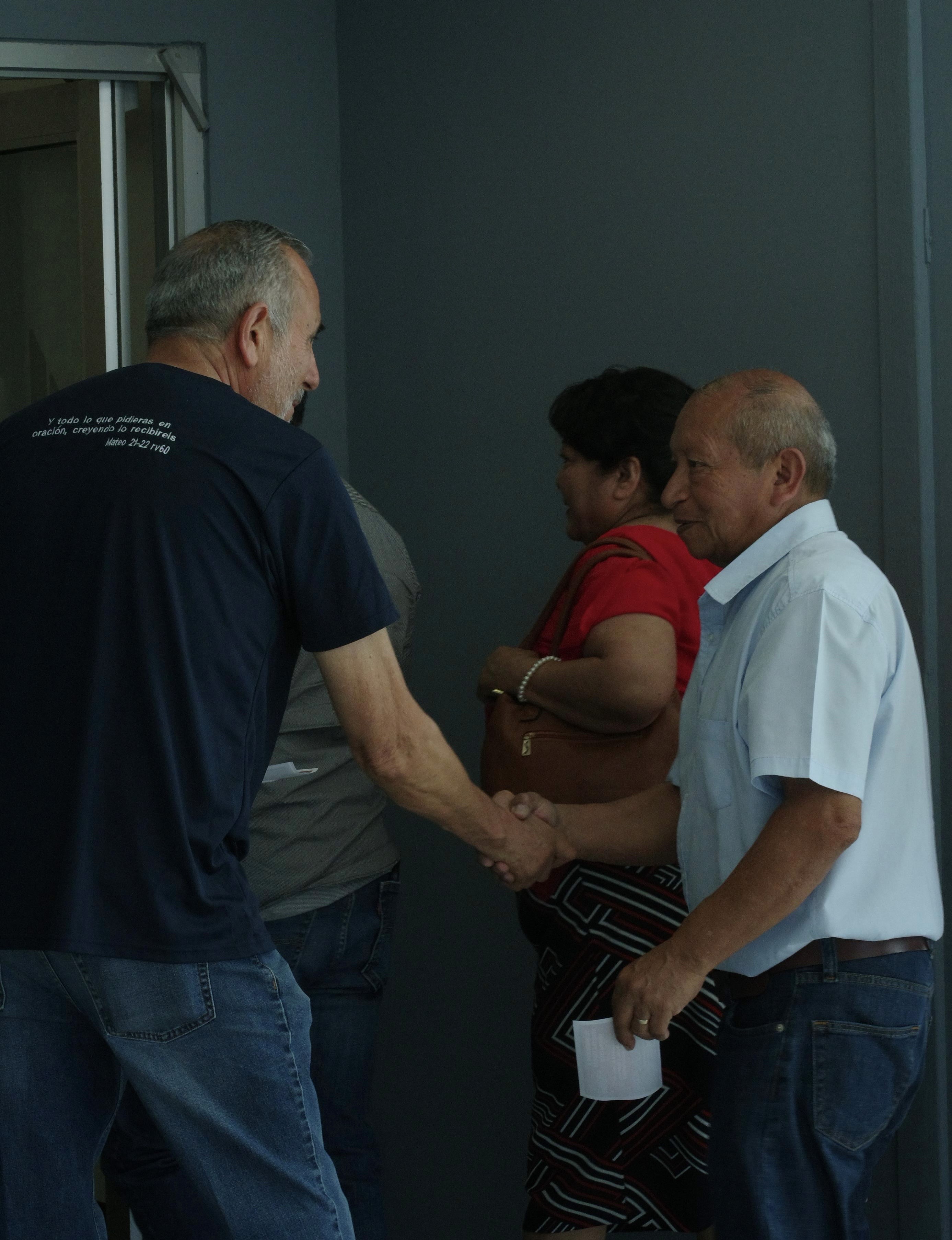 A group of people sitting on grass under trees, enjoying a sunny day near a body of water.