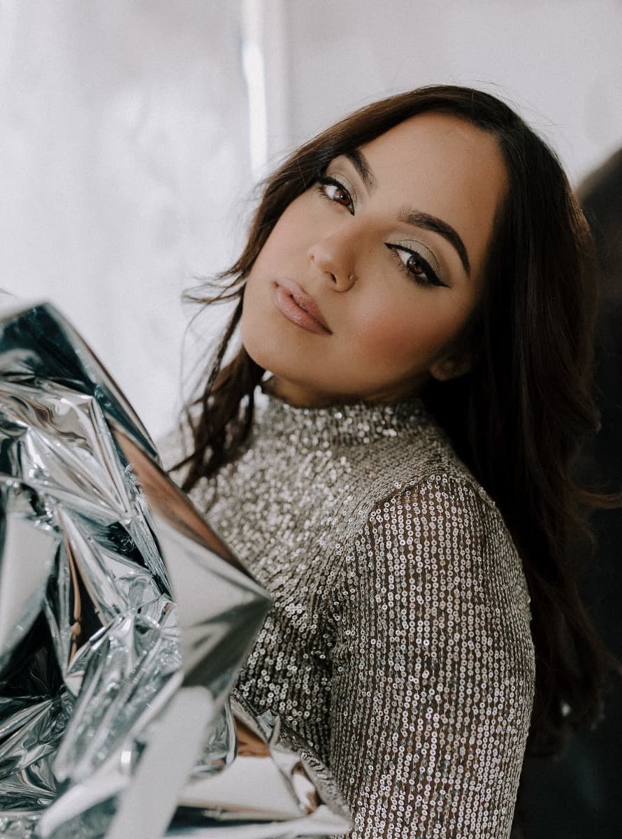 A close-up of a model wearing a sparkling silver top, posing with reflective Mylar, part of a creative shoot at Revelator Studio, a Shreveport natural light photography studio.