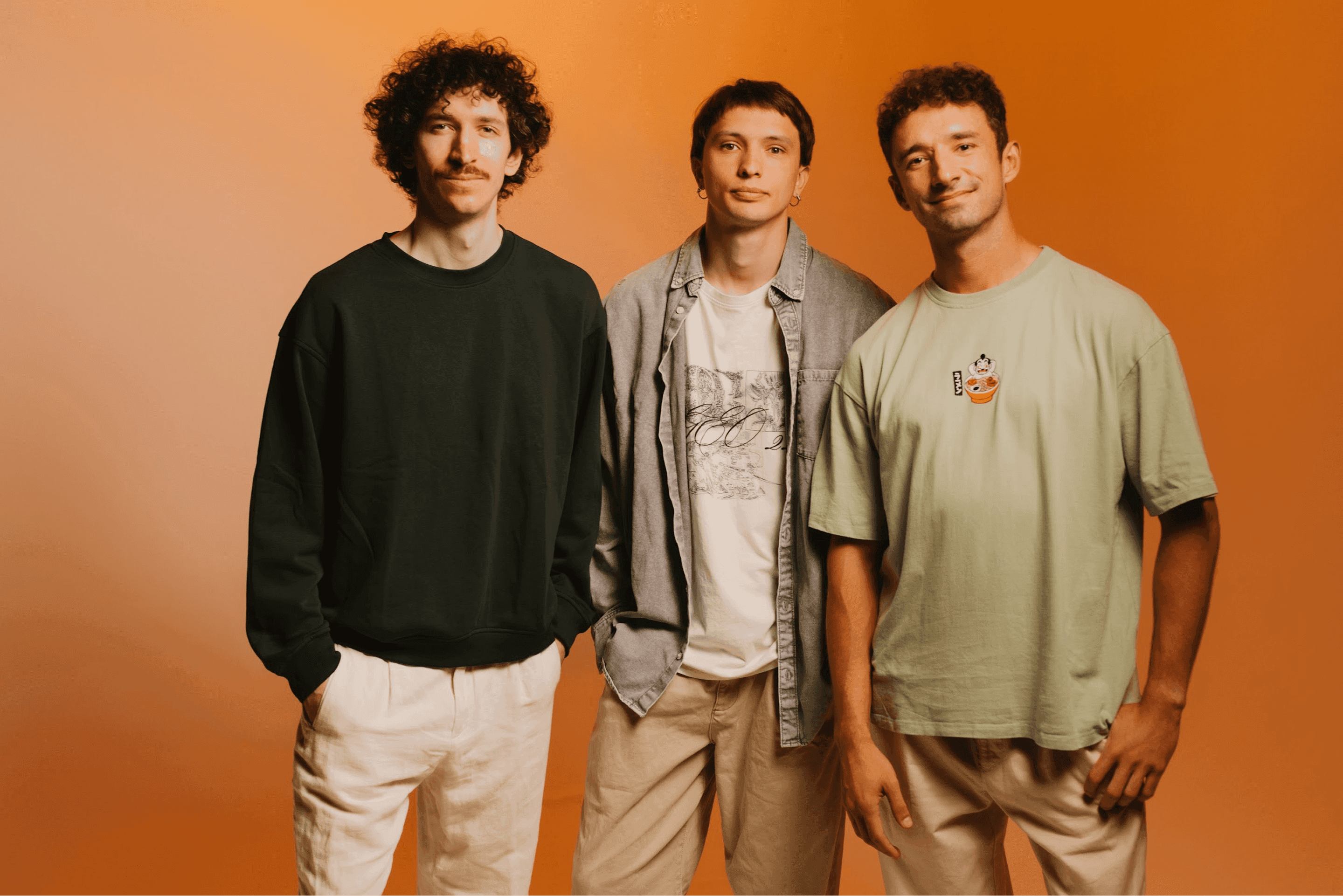 Sergey, Borys, and Ilja in a studio portrait on a warm orange background.