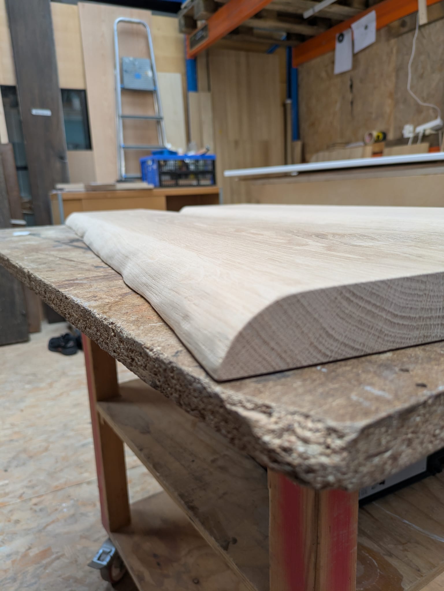 Een onbehandelde eikenhouten wandplank met een afgeronde rand in een houtbewerkingsatelier