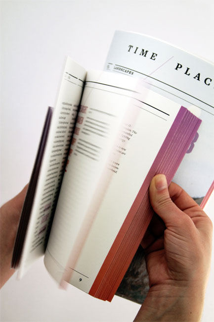 A hand holds open a thick, cream-colored book with maroon edges. The pages are filled with text arranged in columns. The book is open to a page displaying “TIME PLACES” at the top right. The background is plain white.
