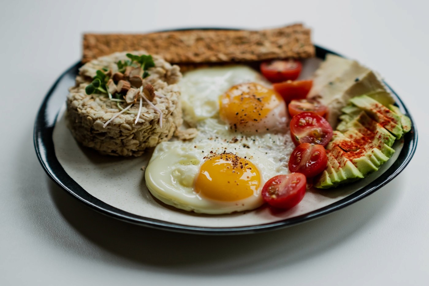 A protein-forward plate with fried eggs, hummus, whole-grain crackers, cherry tomatoes and avocado