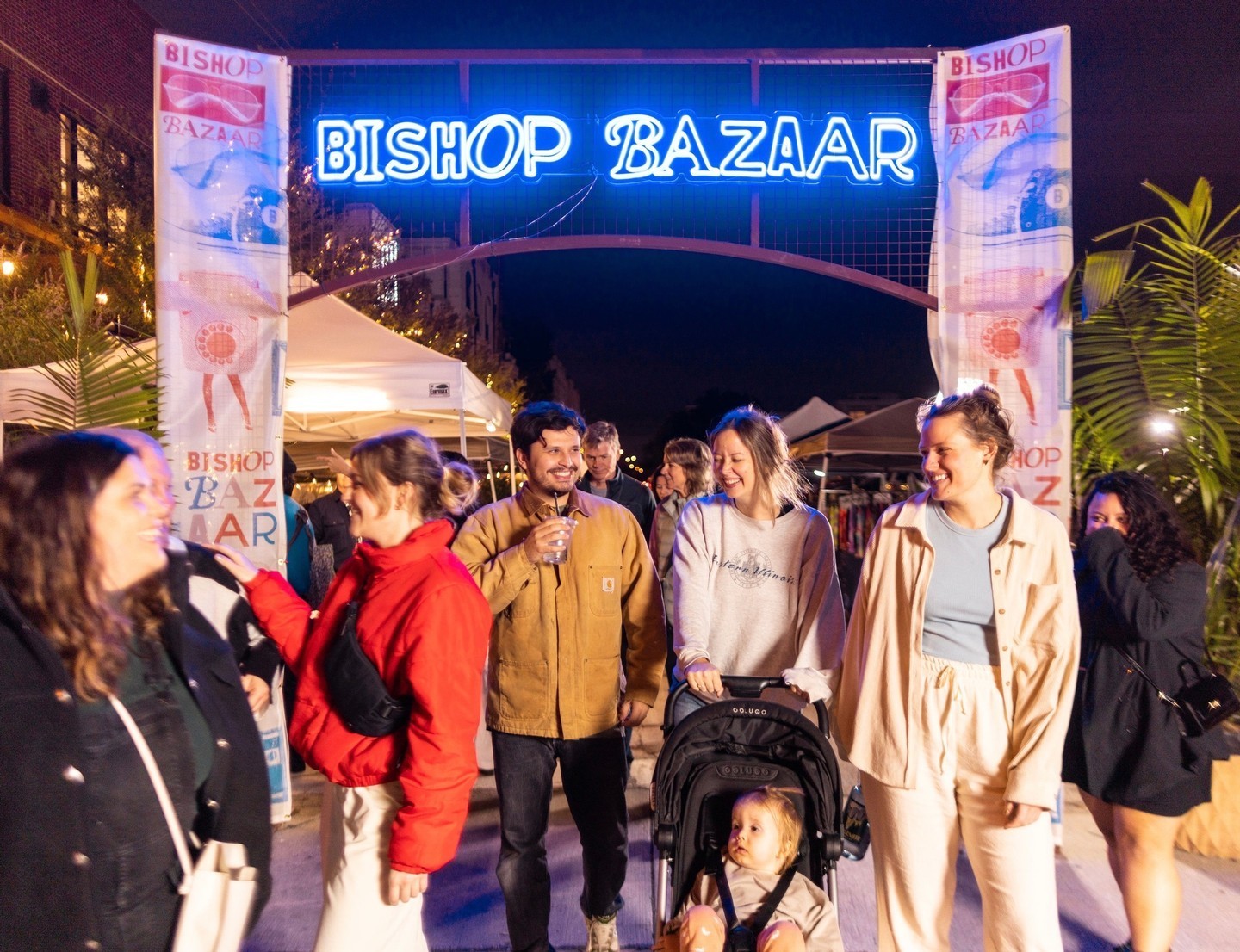 The Bishop Bazaar banner hanging overtop a group of people walking underneath, smiling and walking together