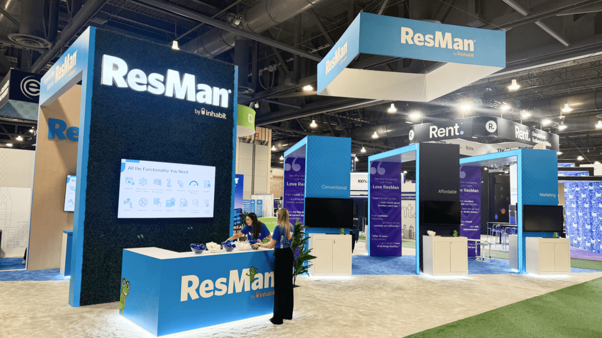 ResMan NAA 2024 large island booth with city-themed wall graphics, meeting area, blue brand panels, hanging signage, and property management software presentation space.