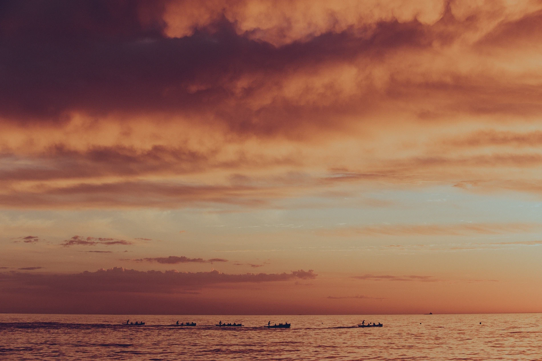 Deep red and orange storm cloud over a calm sea at dusk, with ships anchored on the horizon