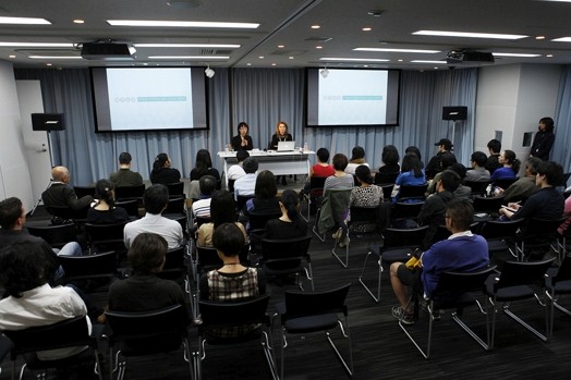 people gathered in a conference room and two women are presenting to the public