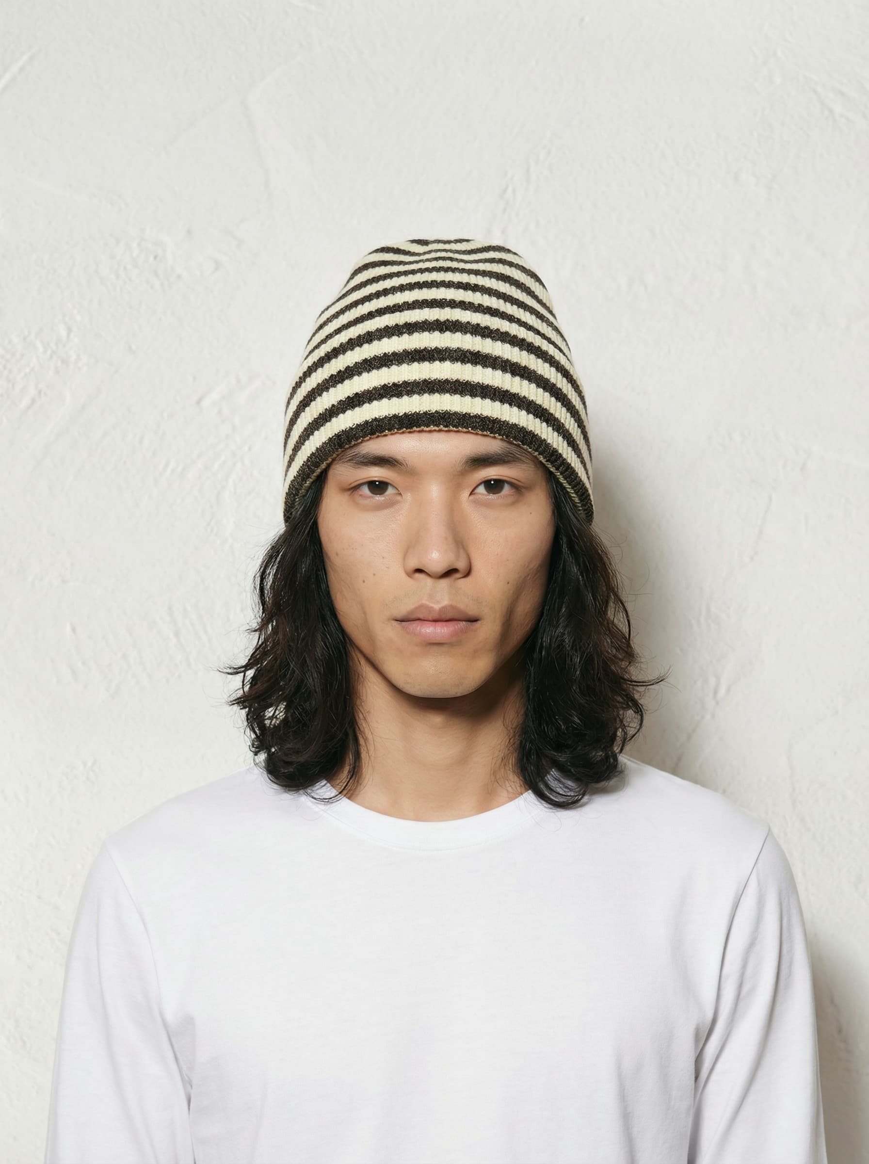 A person wearing a plain white t-shirt, black jeans, and a black cap stands against a neutral background.