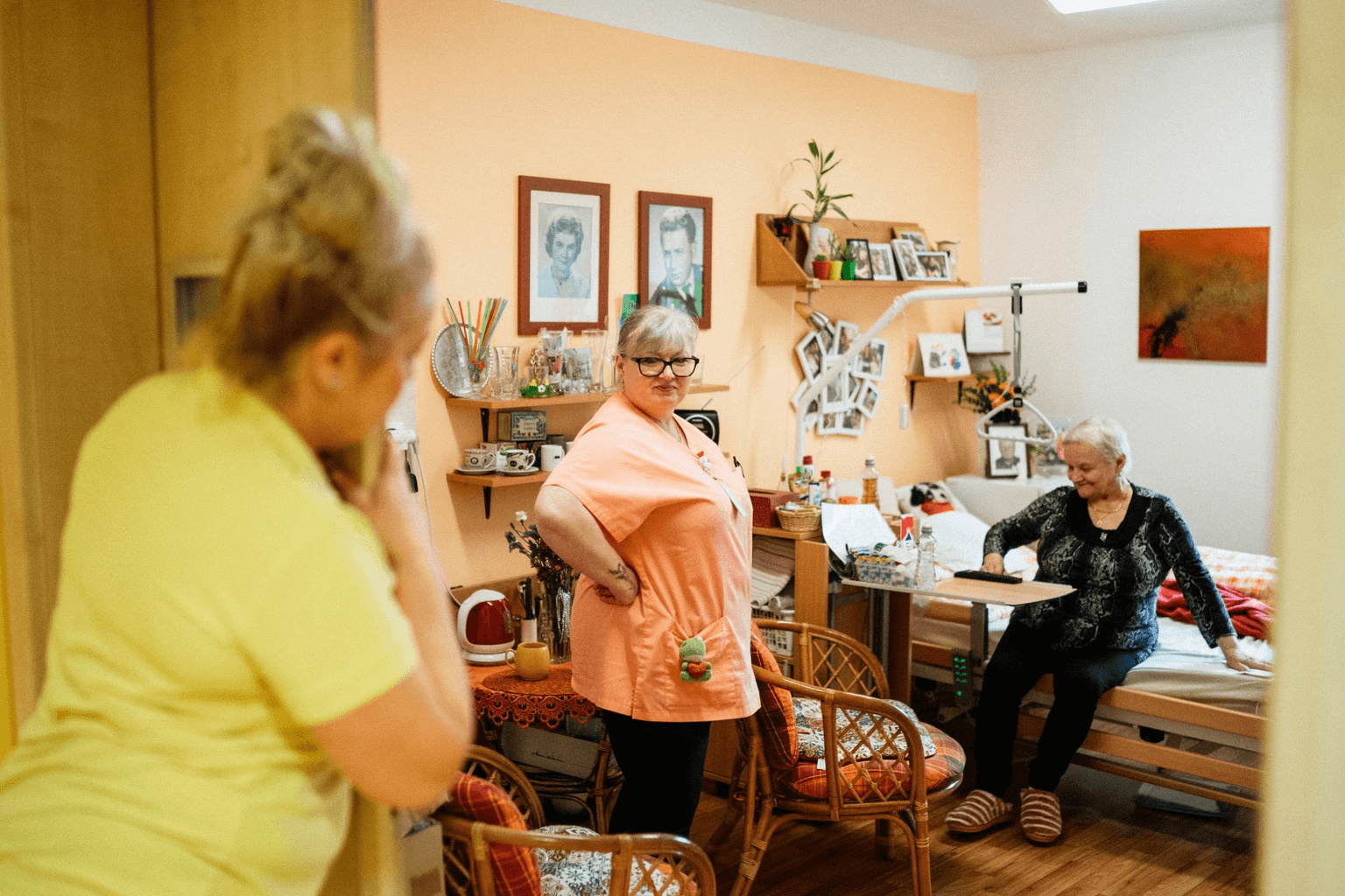 A care worker talking with a resident in her own room, family photographs on the wall.
