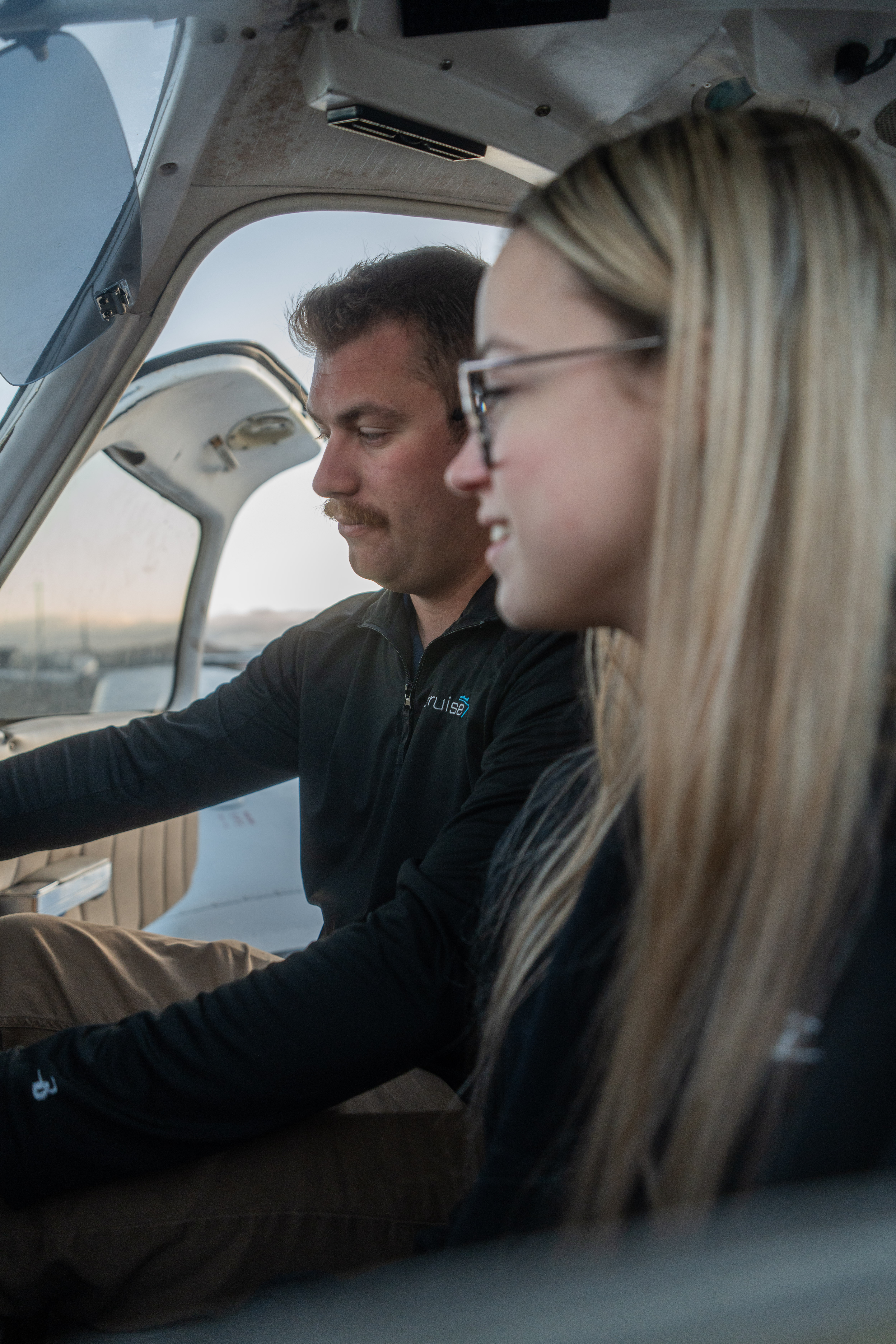 Man wearing headphones and a white t-shirt working on a laptop in soft natural light, with window shadows cast on the wall.
