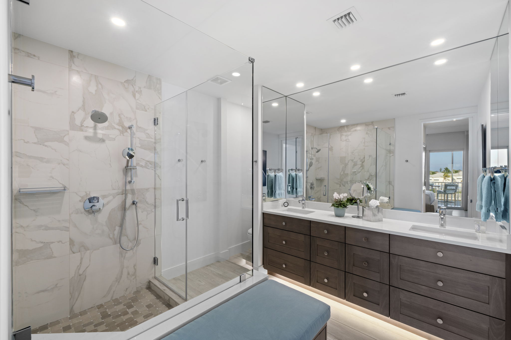 a high-end bathroom with dark cabinets, white walls and tile, and a long mirror spanning the entire bathroom