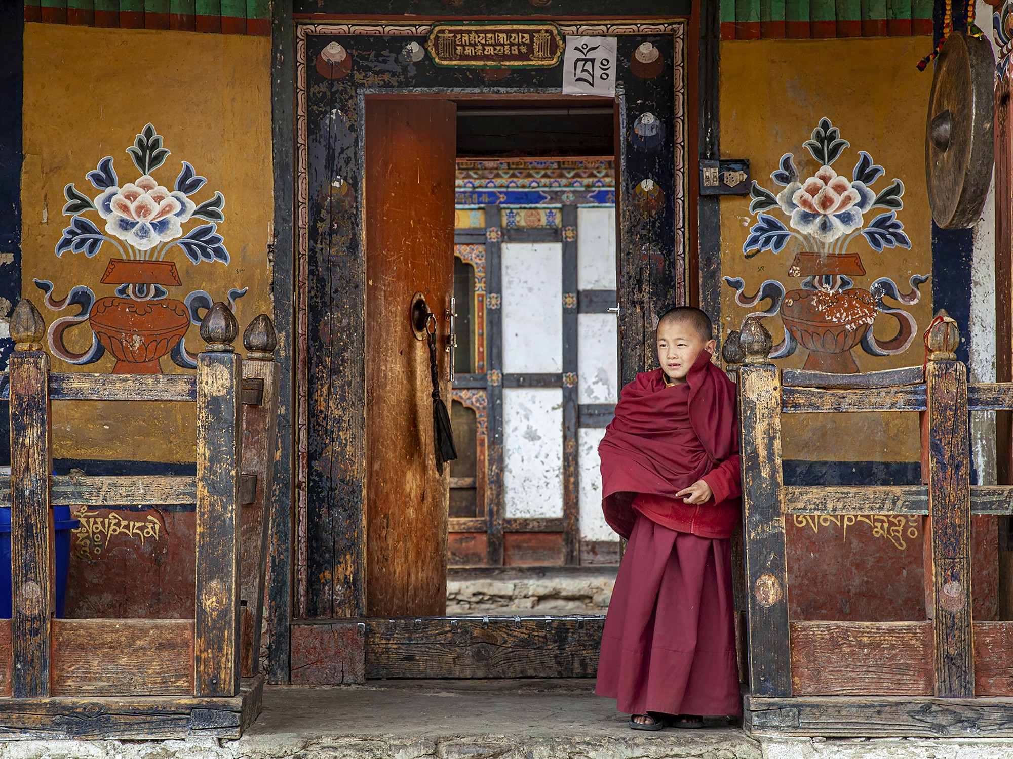 A group of Bhutanese monks stand gracefully at a fence, their serene expressions and traditional robes reflecting a quiet nobility.