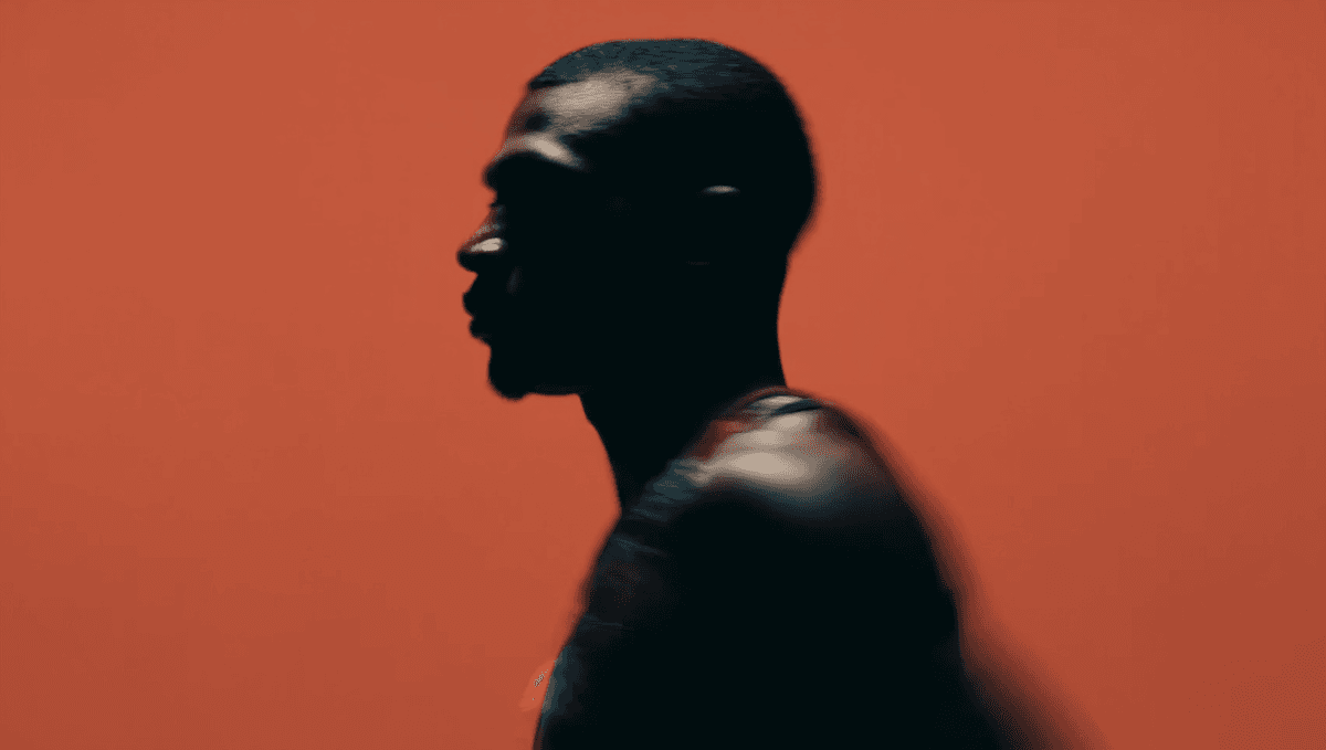 A silhouette of a person in profile against a bold red-orange background, captured with motion blur for a dynamic, artistic effect.