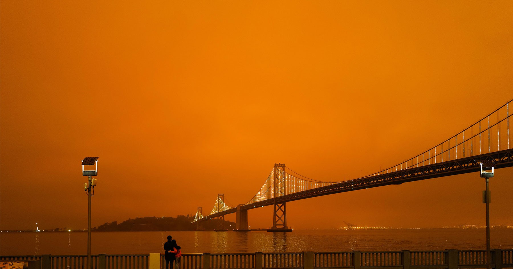 A silhouetted bridge against a dramatic orange sky, creating an eerie, atmospheric scene.