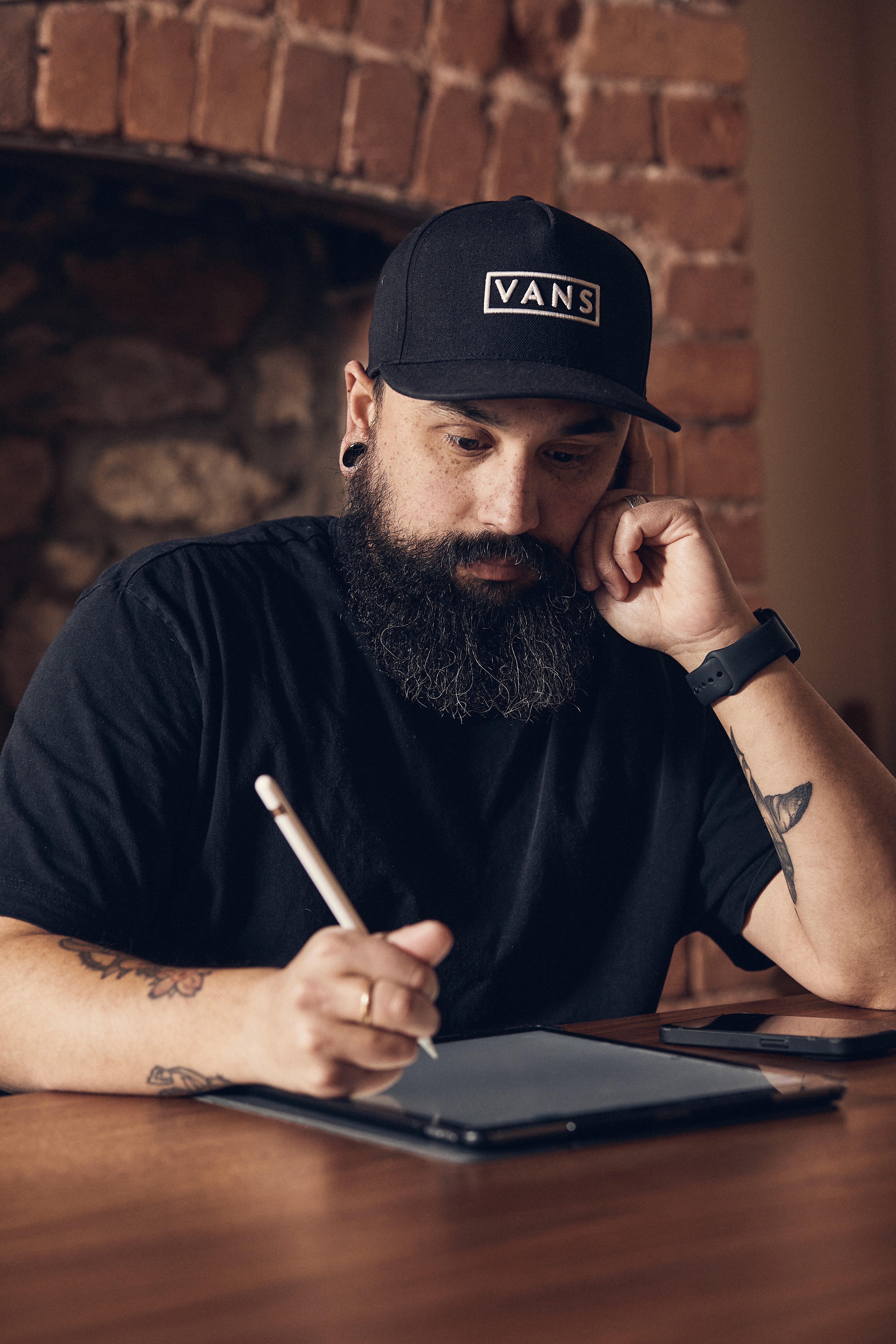 A man drawing on a ipad, with a beard and tattoos