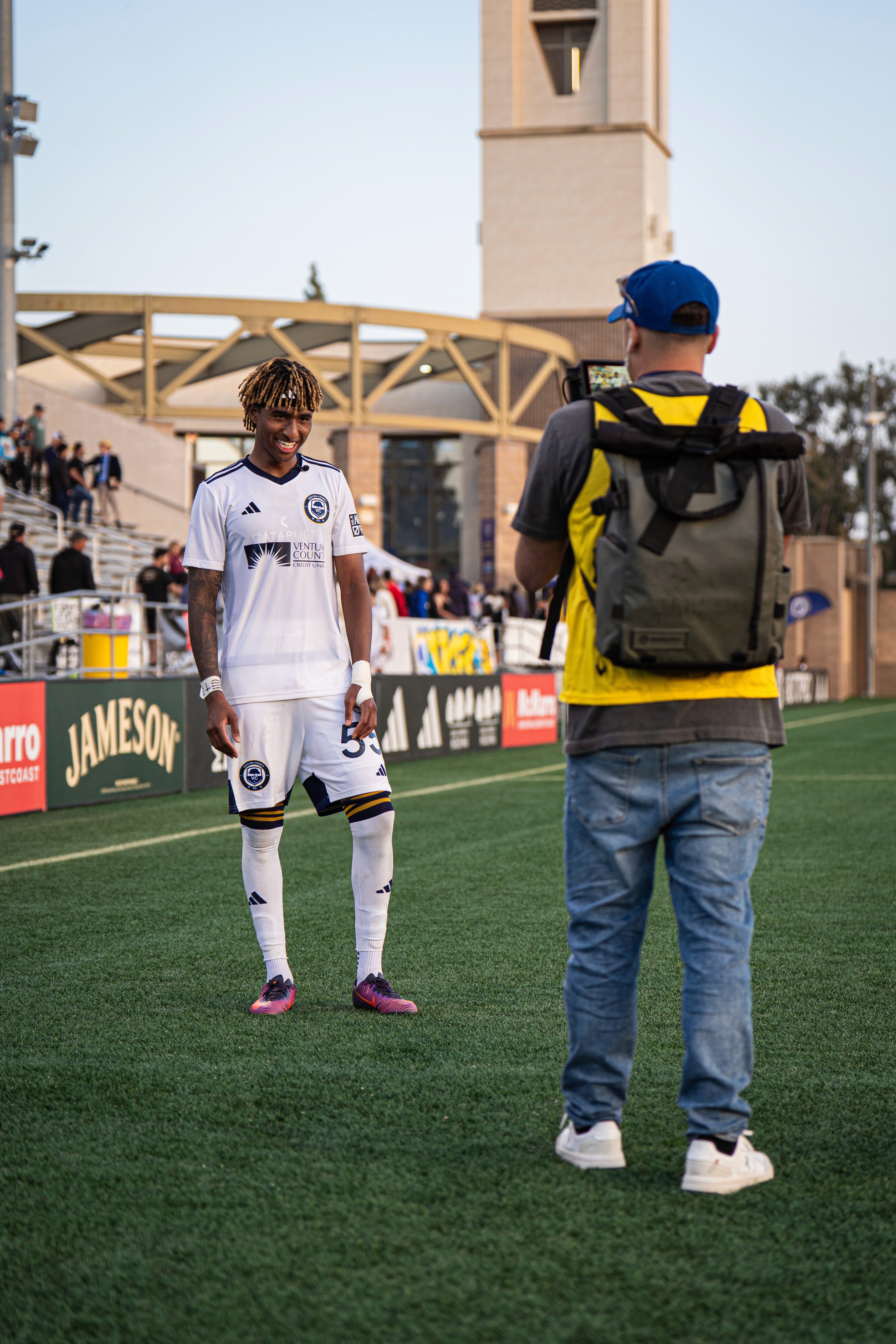 A woman stands beside an old projector, gazing at the camera. The scene is lit with teal and red hues, creating a mysterious and artistic atmosphere.