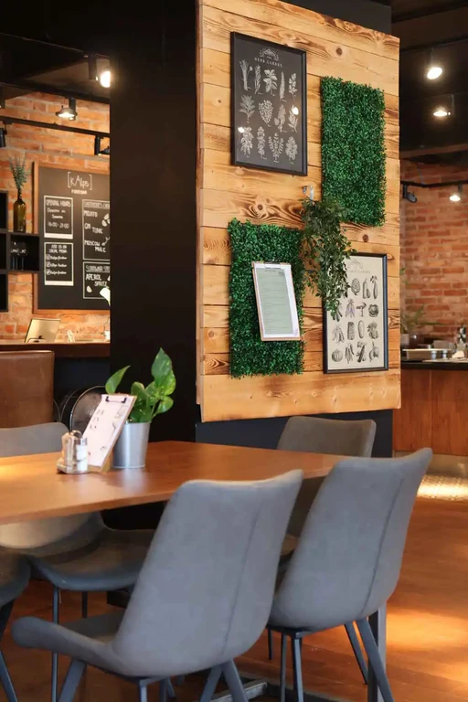Gemütlicher Innenbereich von kAlps mit Holztischen, gepolsterten Stühlen, Pflanzen und botanischen Wandbildern.