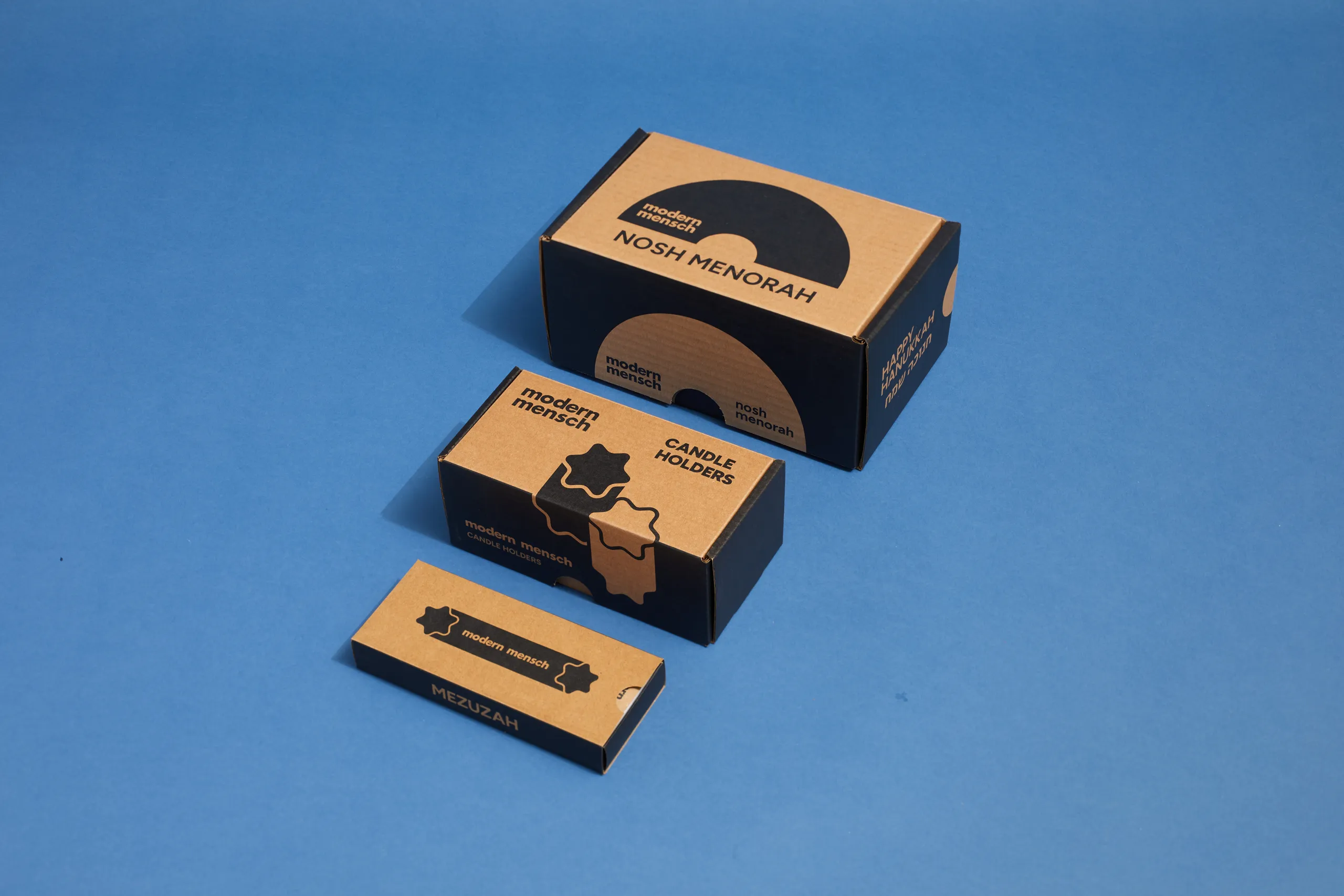 Modern Mensch Nosh Menorah, candle holder, and Mezuzah packages arranged on blue