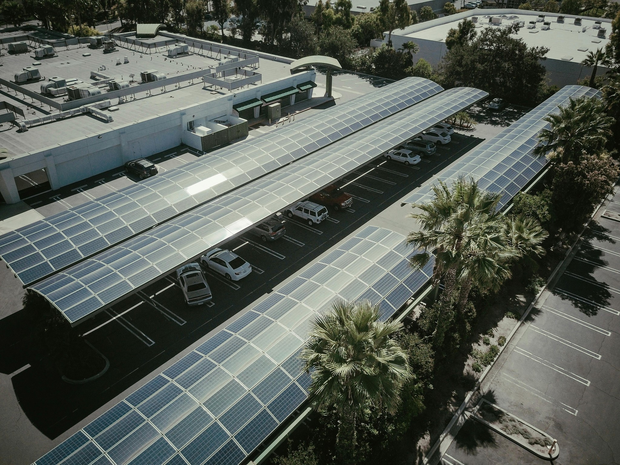  Aerial view of a parking lot with cars under solar panel canopies, surrounded by trees.