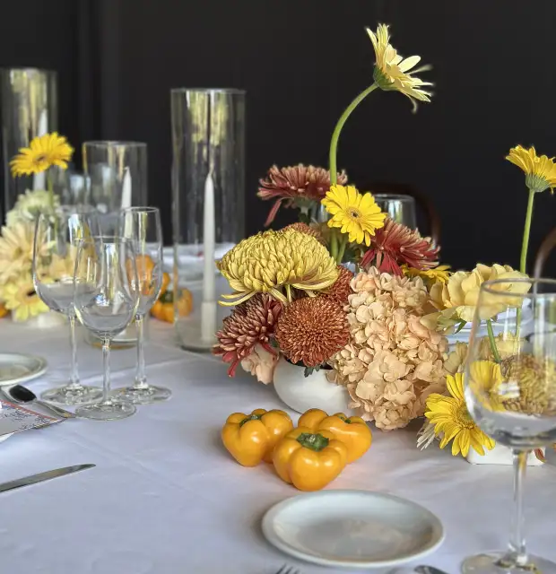 Mesa elegante con centros florales en tonos amarillos y durazno, velas altas y mini pimientos decorativos para ambientación cálida y moderna.