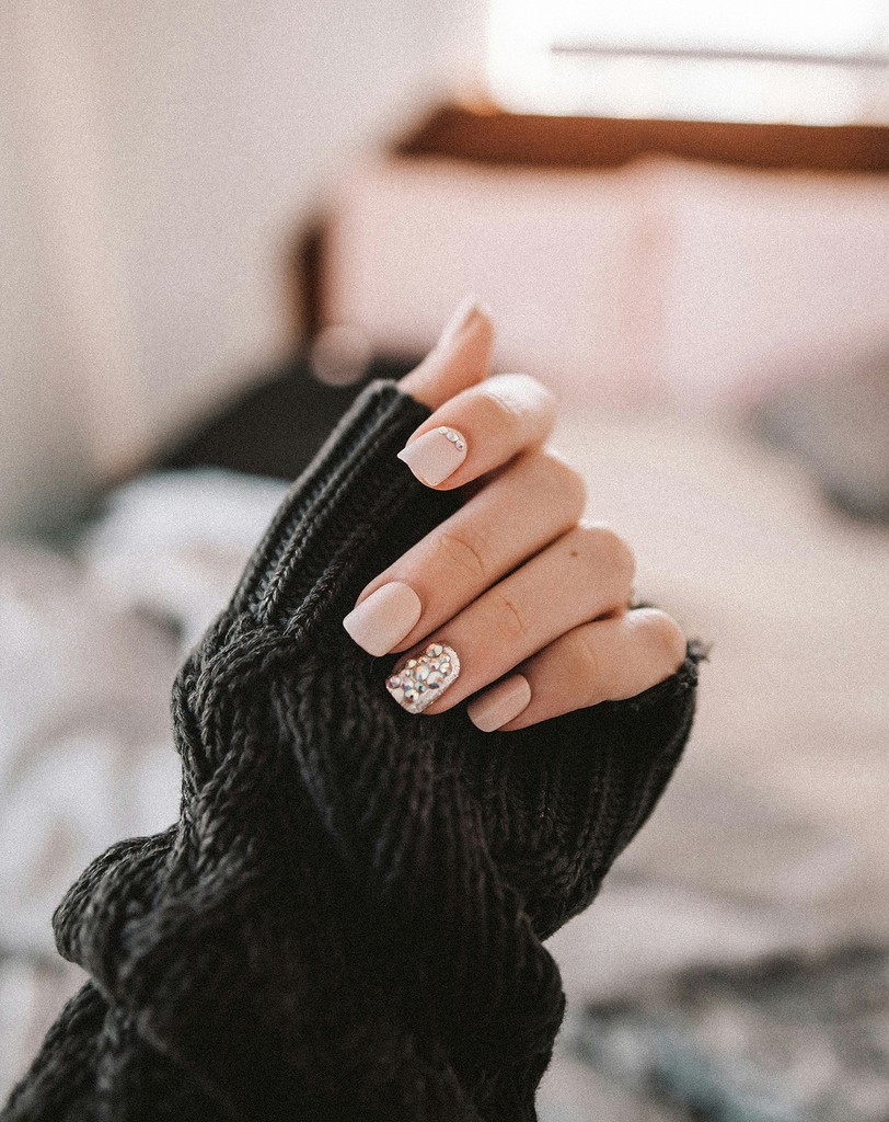 Hand with nude and glittery rhinestone nails in a sweater