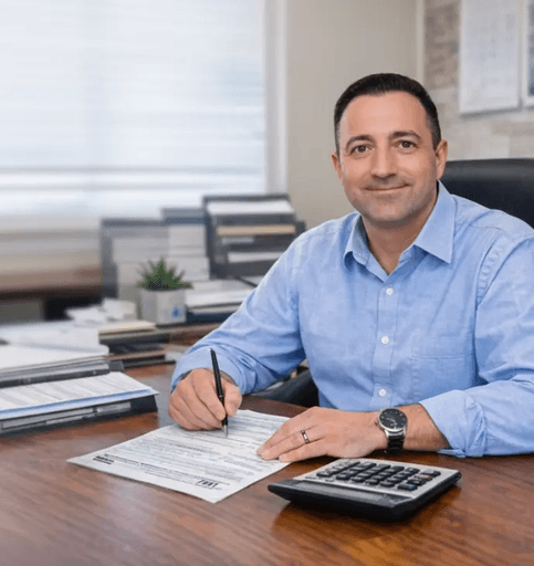 Man in blue shirt filling out tax forms at desk with calculator.