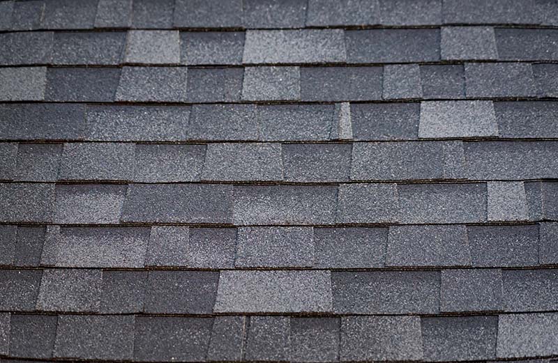 A close-up view of layered wooden shingles in varying shades of gray, arranged in a horizontal pattern.