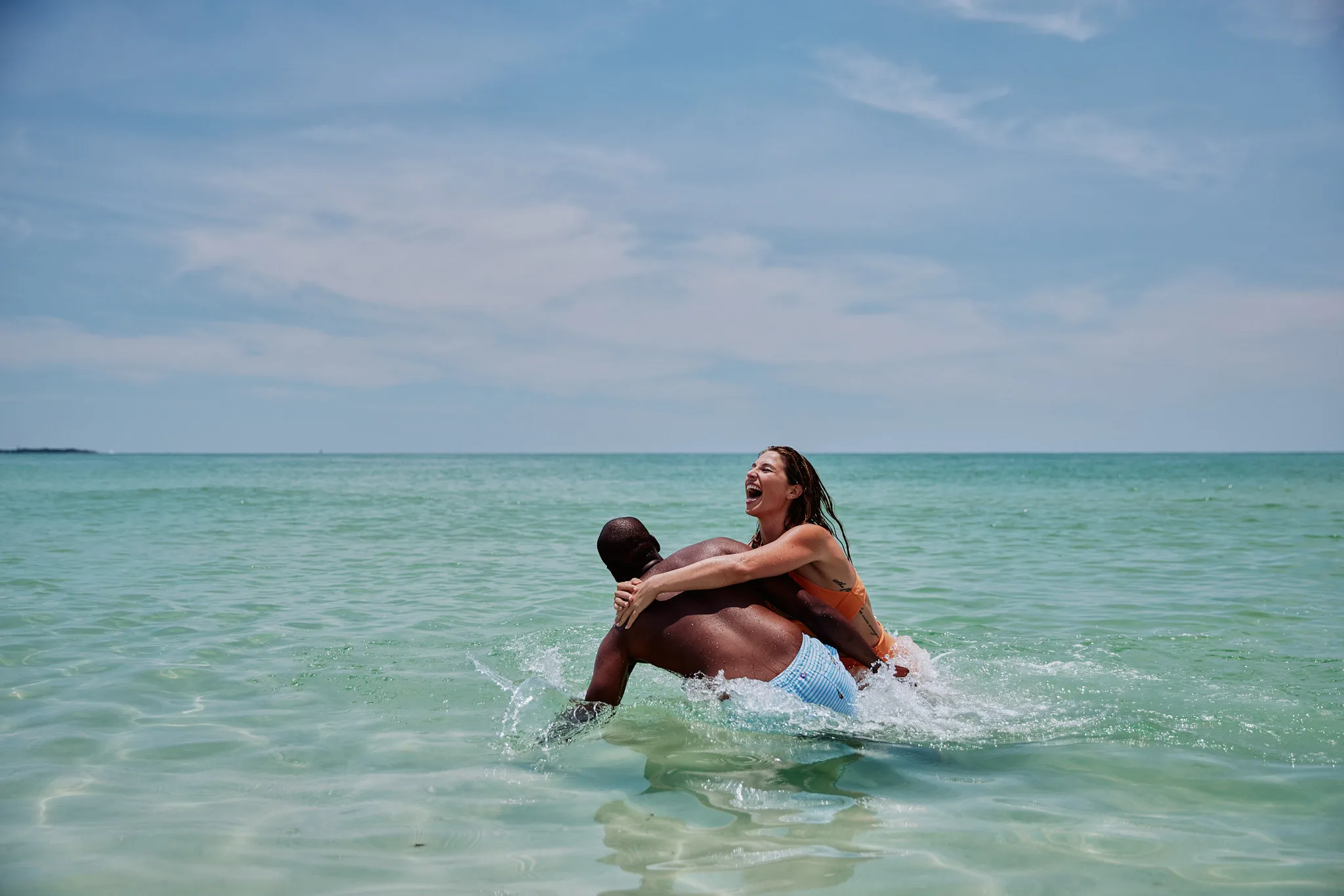 woman climbing onto mans back in ocean — lifestyle photography by Tom Kubik