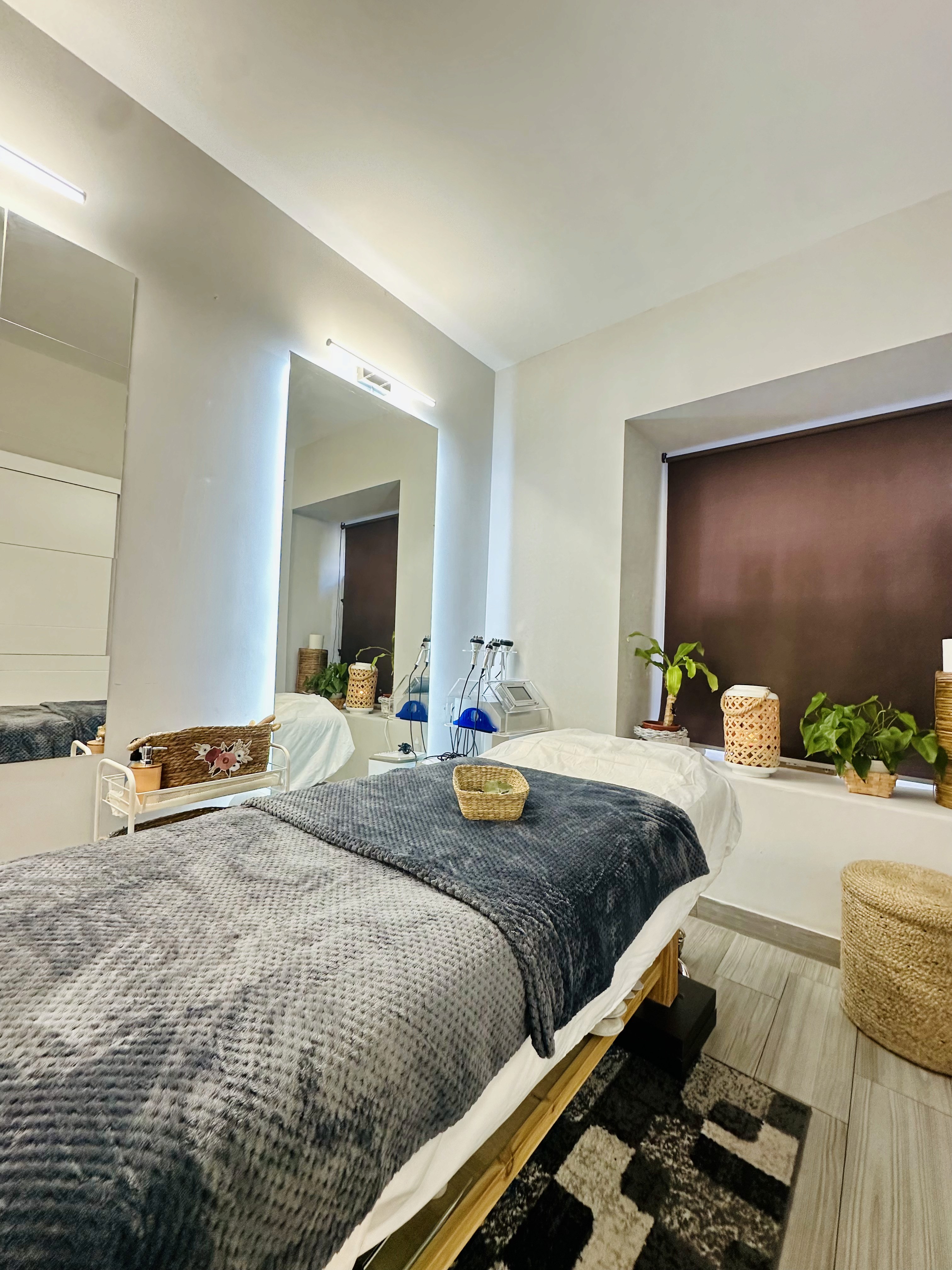 A serene and elegant spa space with wooden reclining chairs and white cushions. Golden sunlight filters through a cascading water feature, creating a peaceful atmosphere. Tropical plants and candles add to the relaxing ambiance.