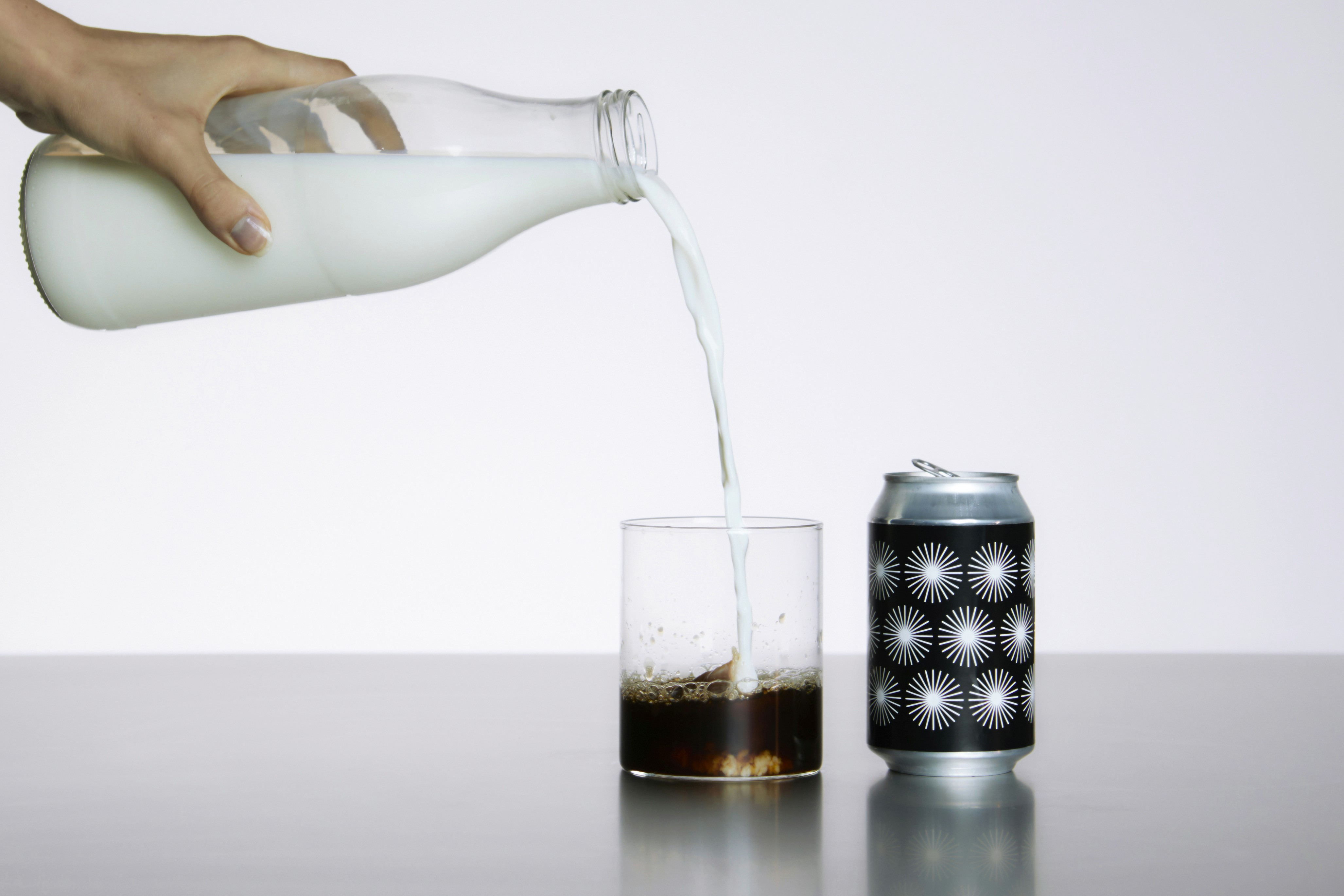 Milch wird in ein Glas mit Cola gegossen, daneben eine Dose mit grafischem Schwarz-Weiß-Muster – Sinnbild für Markenstruktur, visuelle Klarheit und systemische Identität.