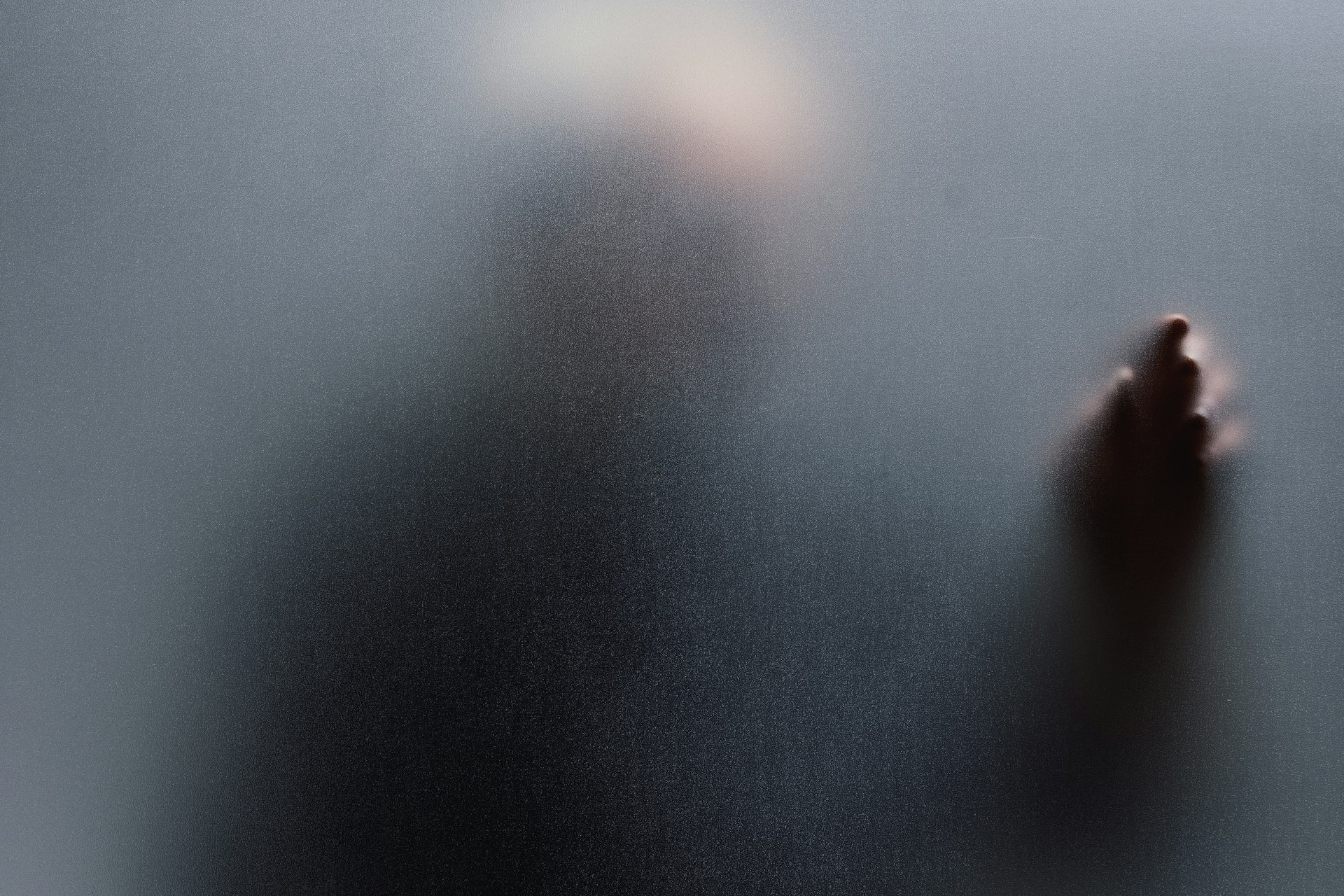 Blurred silhouette of a person standing behind frosted glass with an outstretched hand pressed against the surface, creating a moody, mysterious privacy-themed scene.
