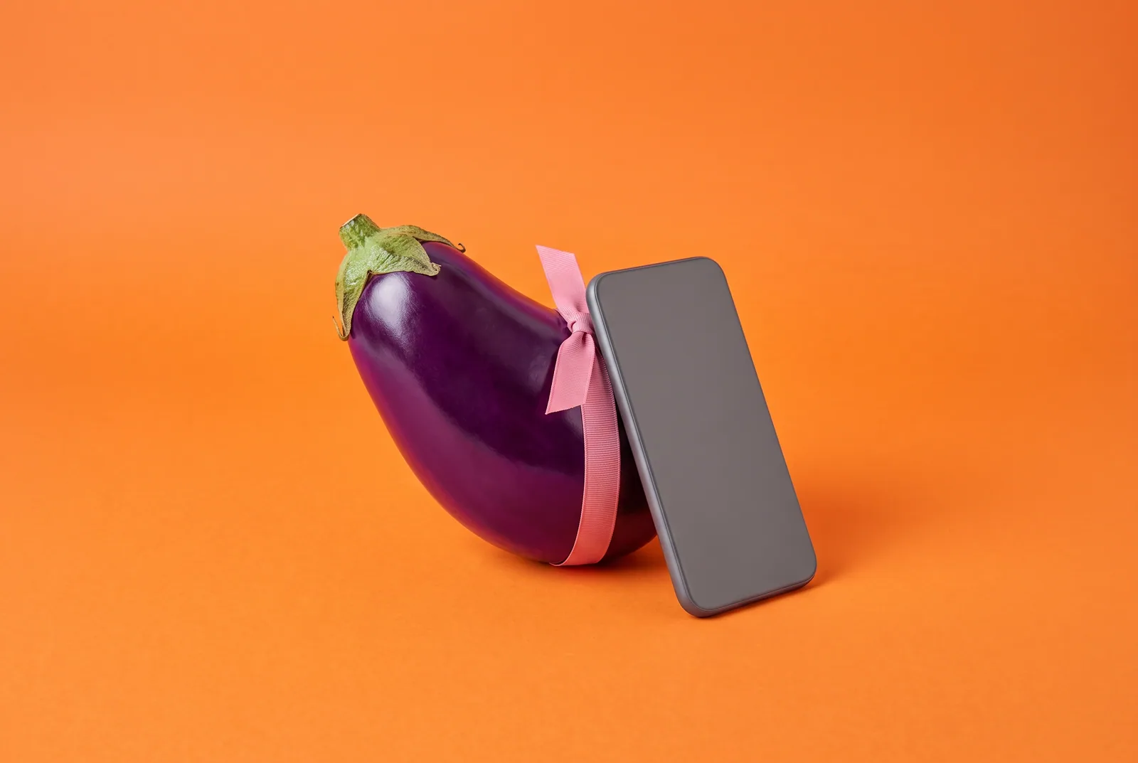 An eggplant tied to a face-down phone with a pink ribbon, signs of sexting addiction