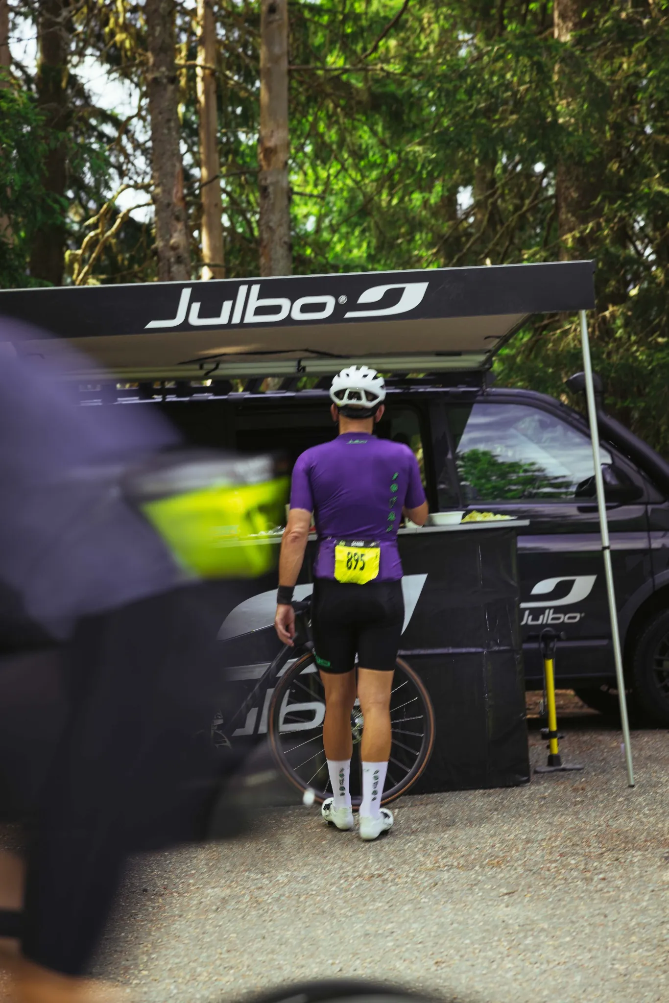 Cyclist of the peloton at the start of L'Étape du Tour - white helmets and purple jerseys under the start banner