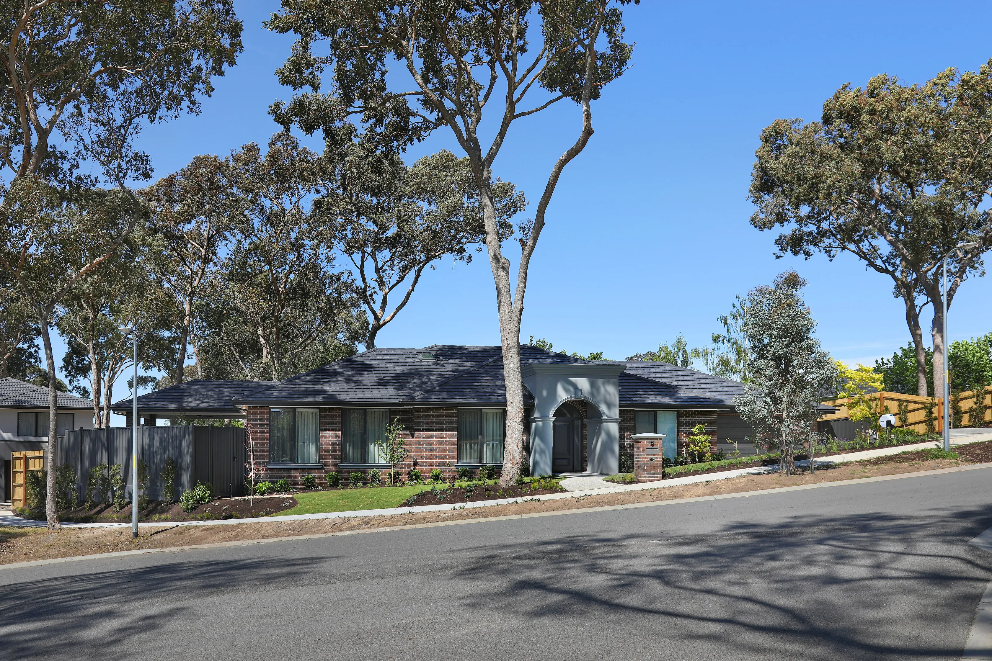 Street view of the Diamond Creek home, a single-storey blend-brick residence with grey tiled roof and rendered arched portico, set behind a landscaped verge among tall gum trees