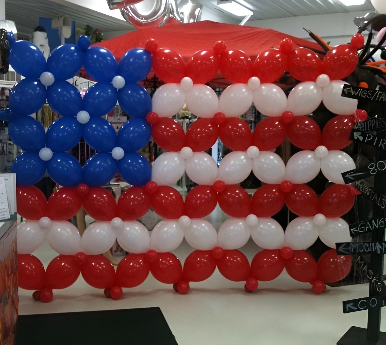 A festive balloon display features a stylized American flag design with alternating rows of red, white, and blue balloons, creating a patriotic backdrop in a celebratory setting.