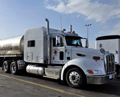 White semi-truck with a tanker trailer parked at a truck stop under a clear sky.