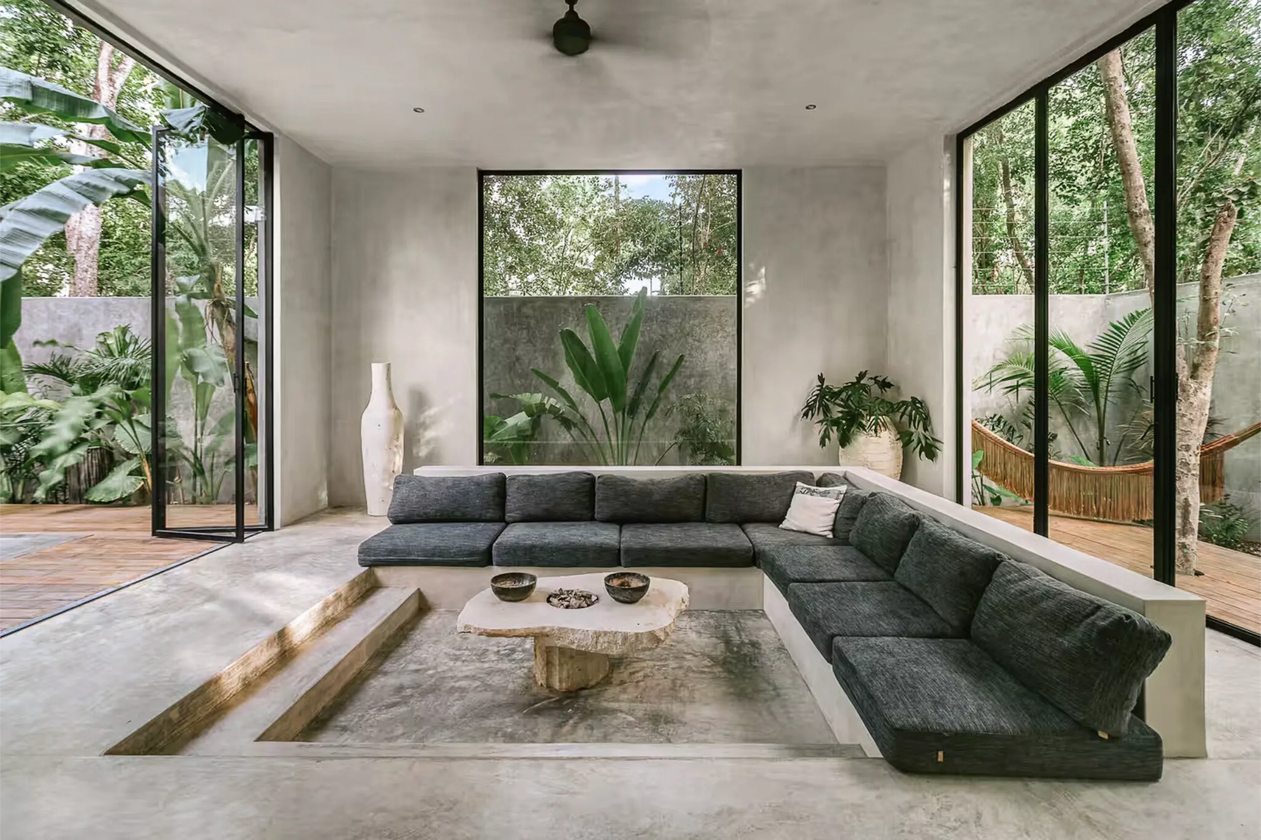 Detail of the conversation pit (sunken living room) with grey upholstery and a raw stone coffee table designed by Arquitectura Mixta.