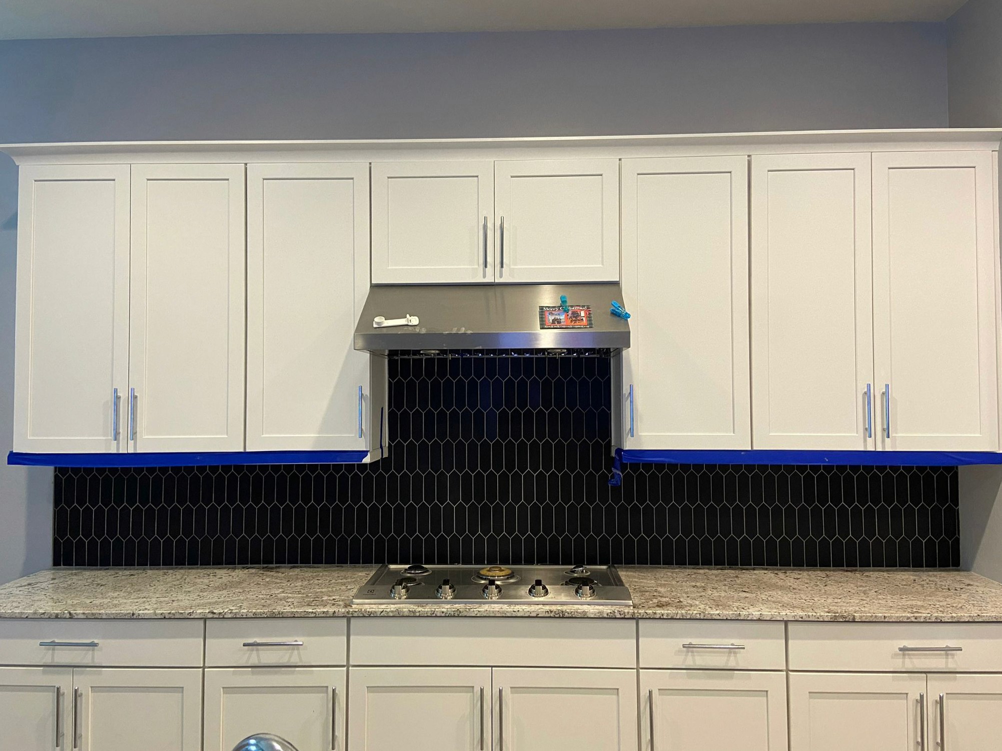 Stylish kitchen with white cabinets, a stainless steel range hood, and a black hexagonal tile backsplash.