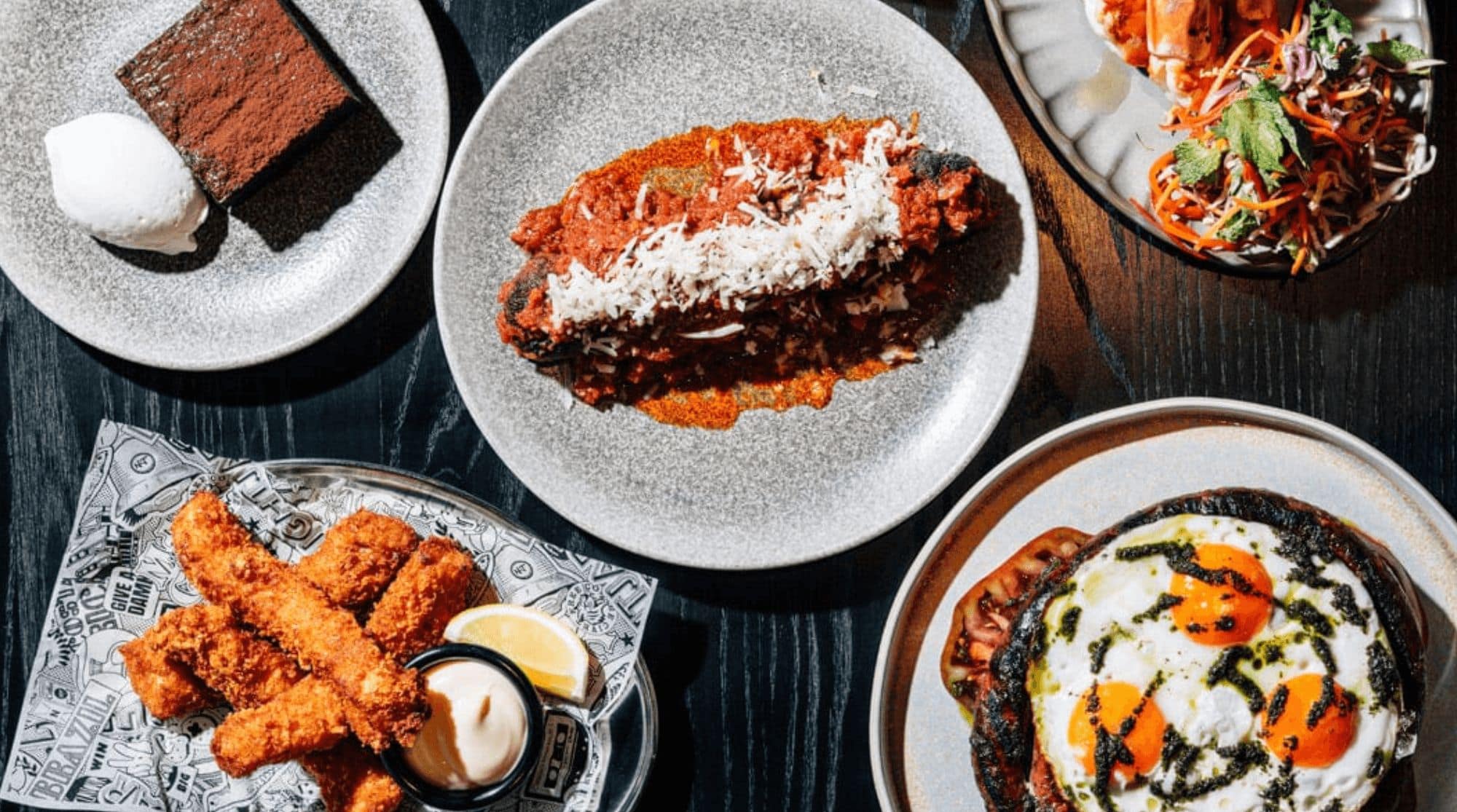 Pasta, chocolate cake, fried fish, and eggs placed on top of a black table in a breakfast place in Dubai.