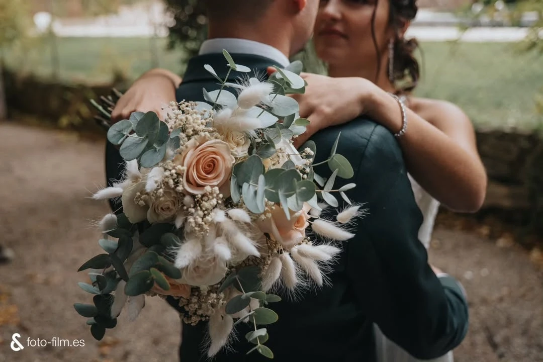 A group of people gather outside a rustic stone building surrounded by lush greenery and flowering plants, bathed in warm, natural sunlight, capturing a serene and welcoming ambiance.
