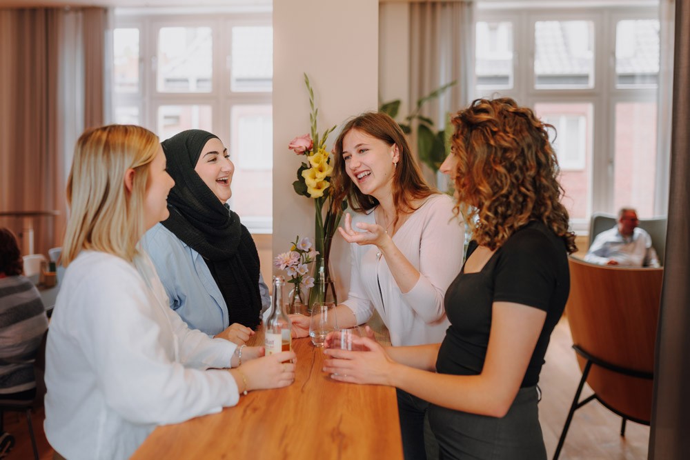 Mehrere Mitarbeiterinnen stehen locker beisammen in einem Besprechungsraum von SLB und unterhalten sich.