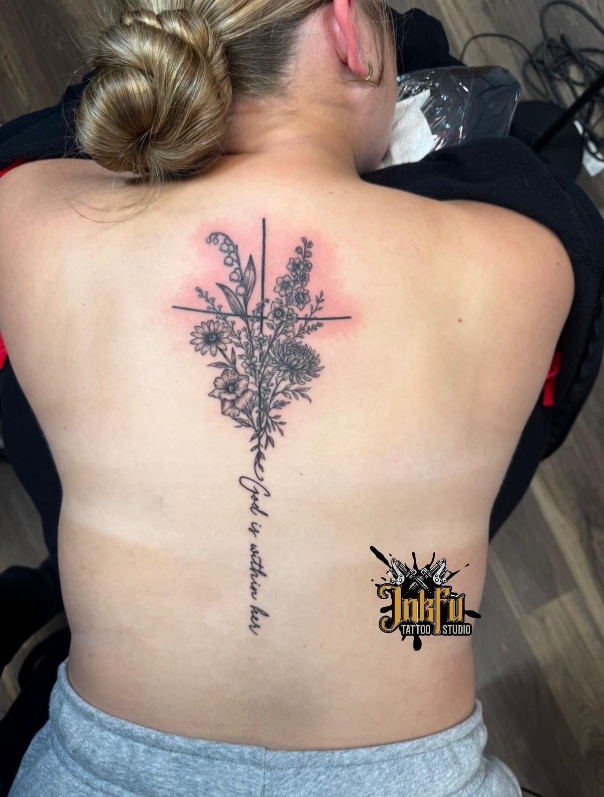 Fine line floral bouquet and cross tattoo with script lettering down the spine, by Meer Rich