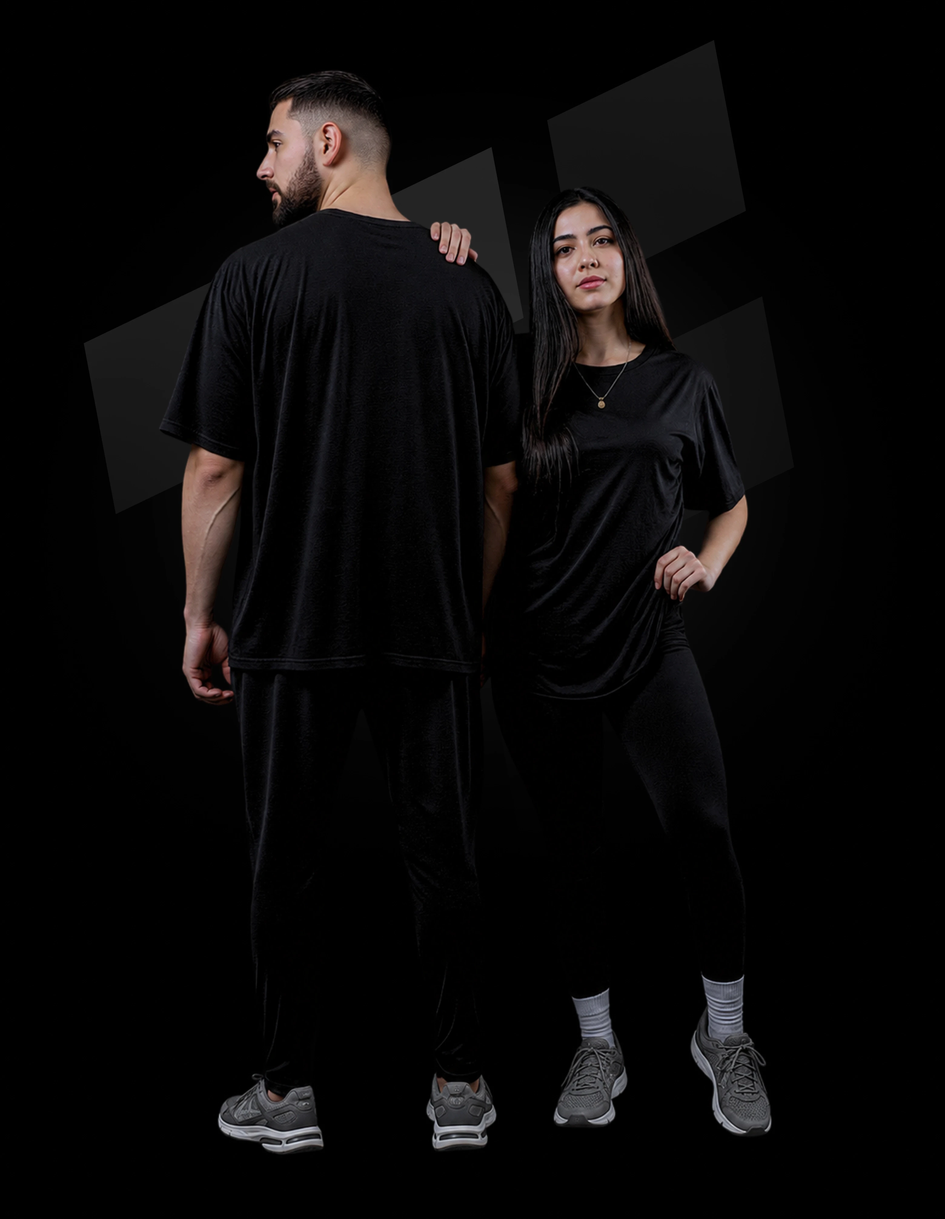 Man and woman in matching black outfits posing. The man is wearing a t-shirt and sweats, and the woman is wearing a black t-shirt and leggings.