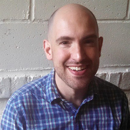 men with square shirt in front of brick wall