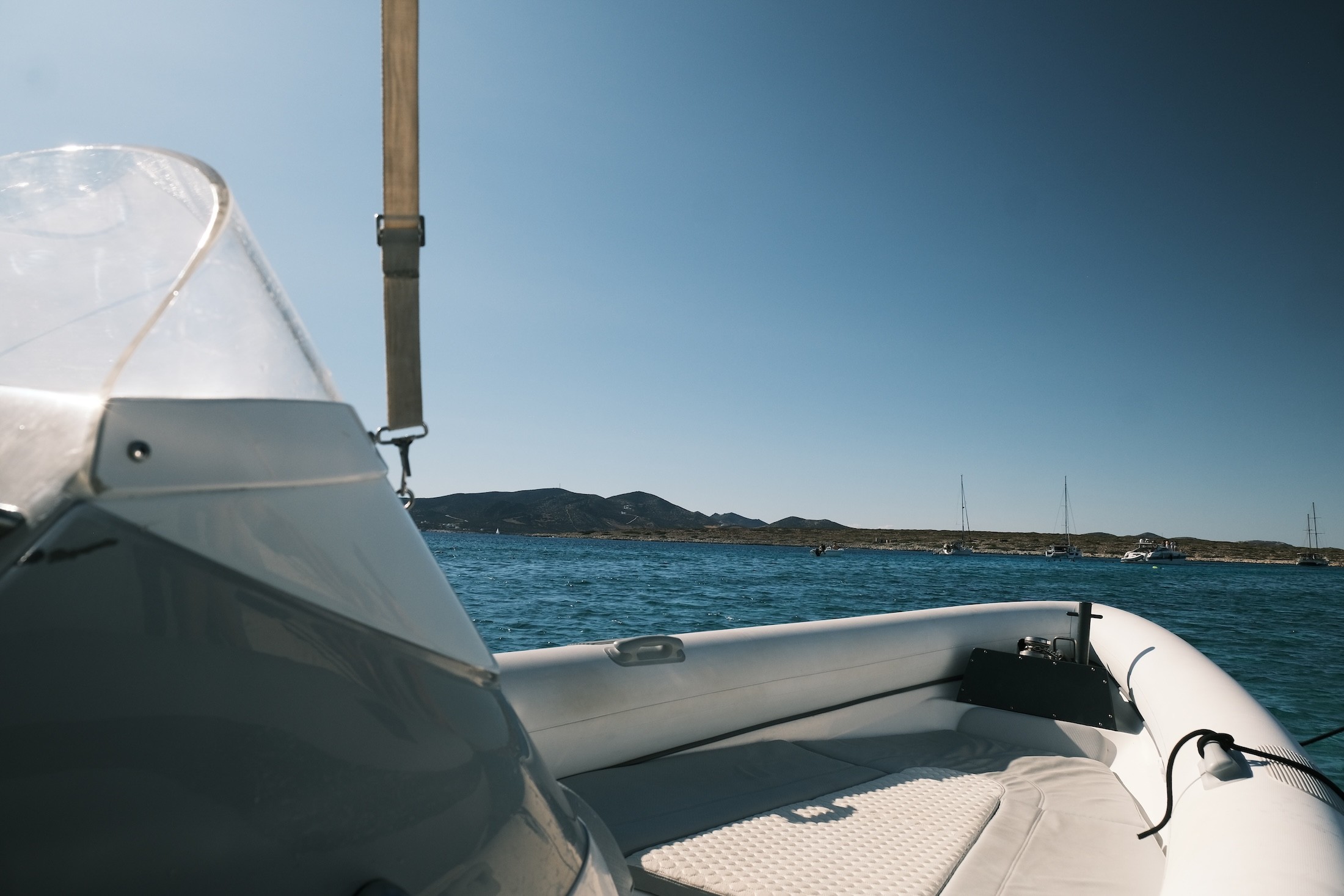 White Rock 36 speedboat with captain at helm cruising calm blue waters near Paros coastline with hills in background.
