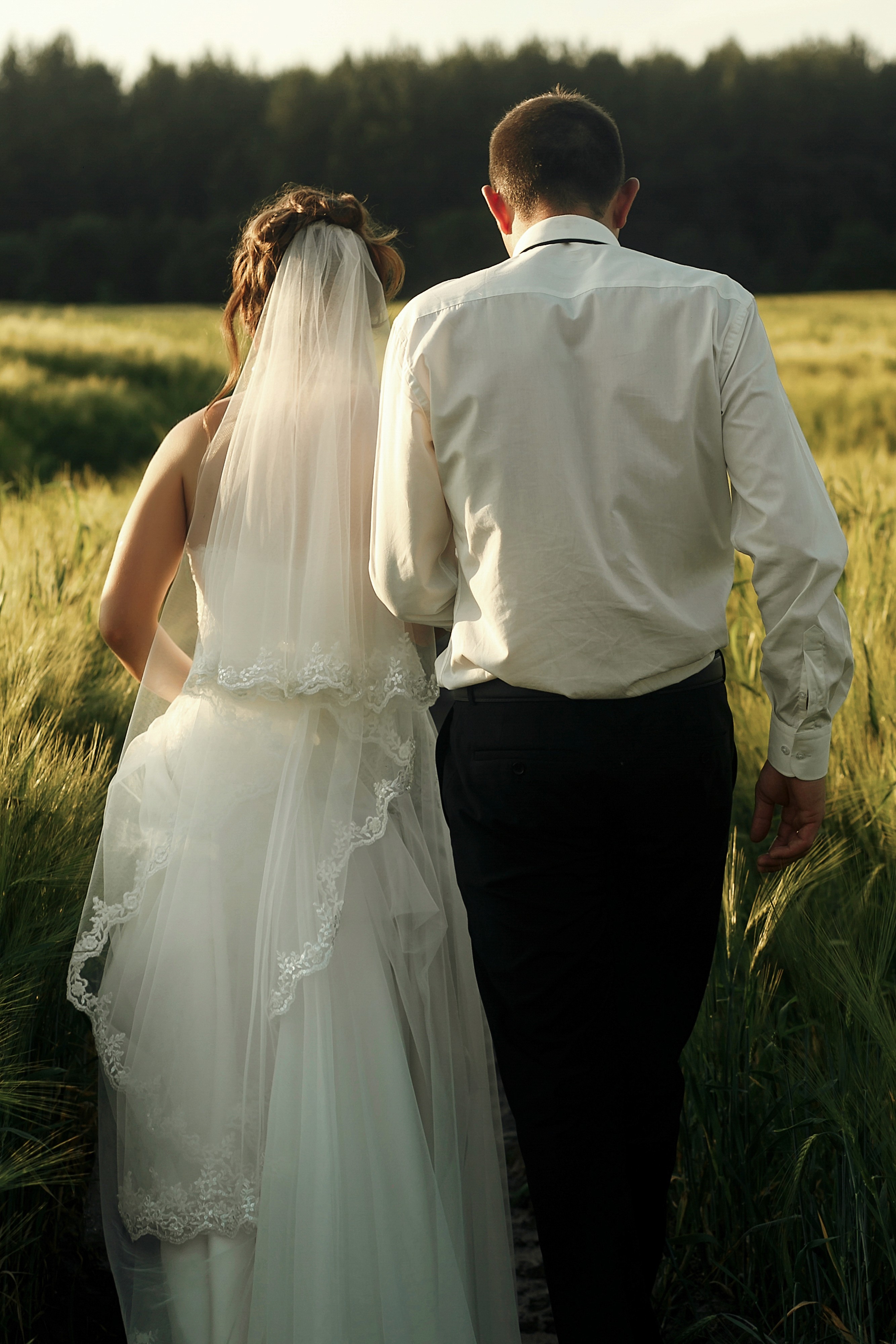 Bride and groom walking through golden wheat field at sunset