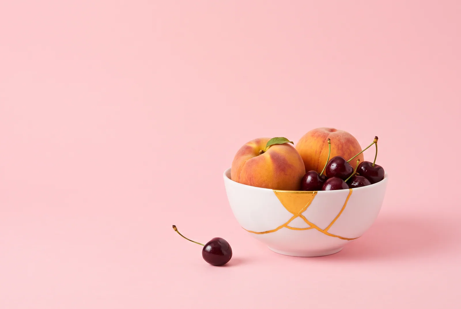 Cracked ceramic bowl repaired with gold kintsugi seams holding fresh peaches and cherries, symbolizing rebuilding trust after telling your wife about porn addiction