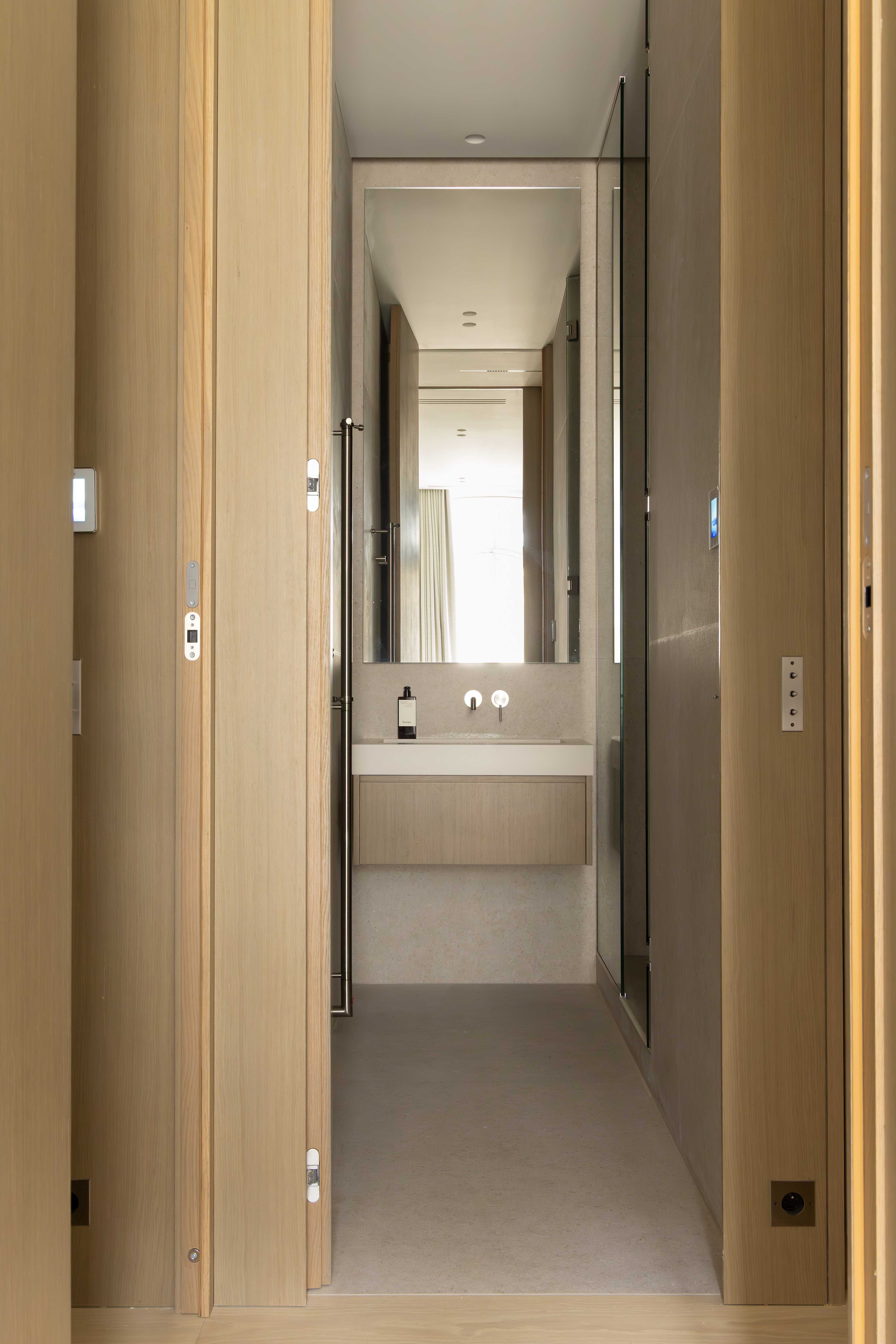 Couloir etroit en bois clair menant a la salle de bain, avec rangements integres et miroir au fond